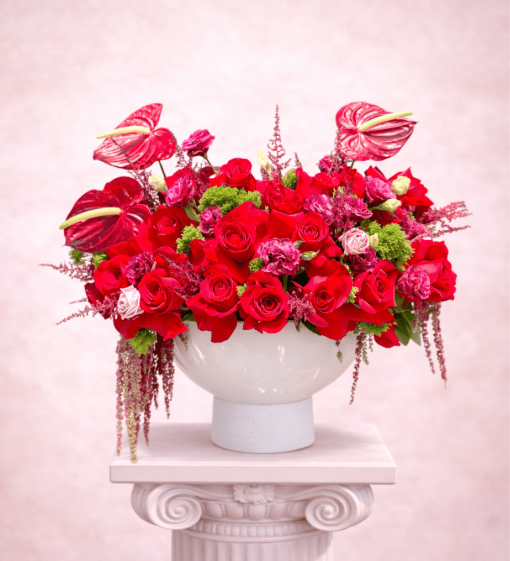 Red rose arrangement in a white pedestal vase with pink anthuriums
