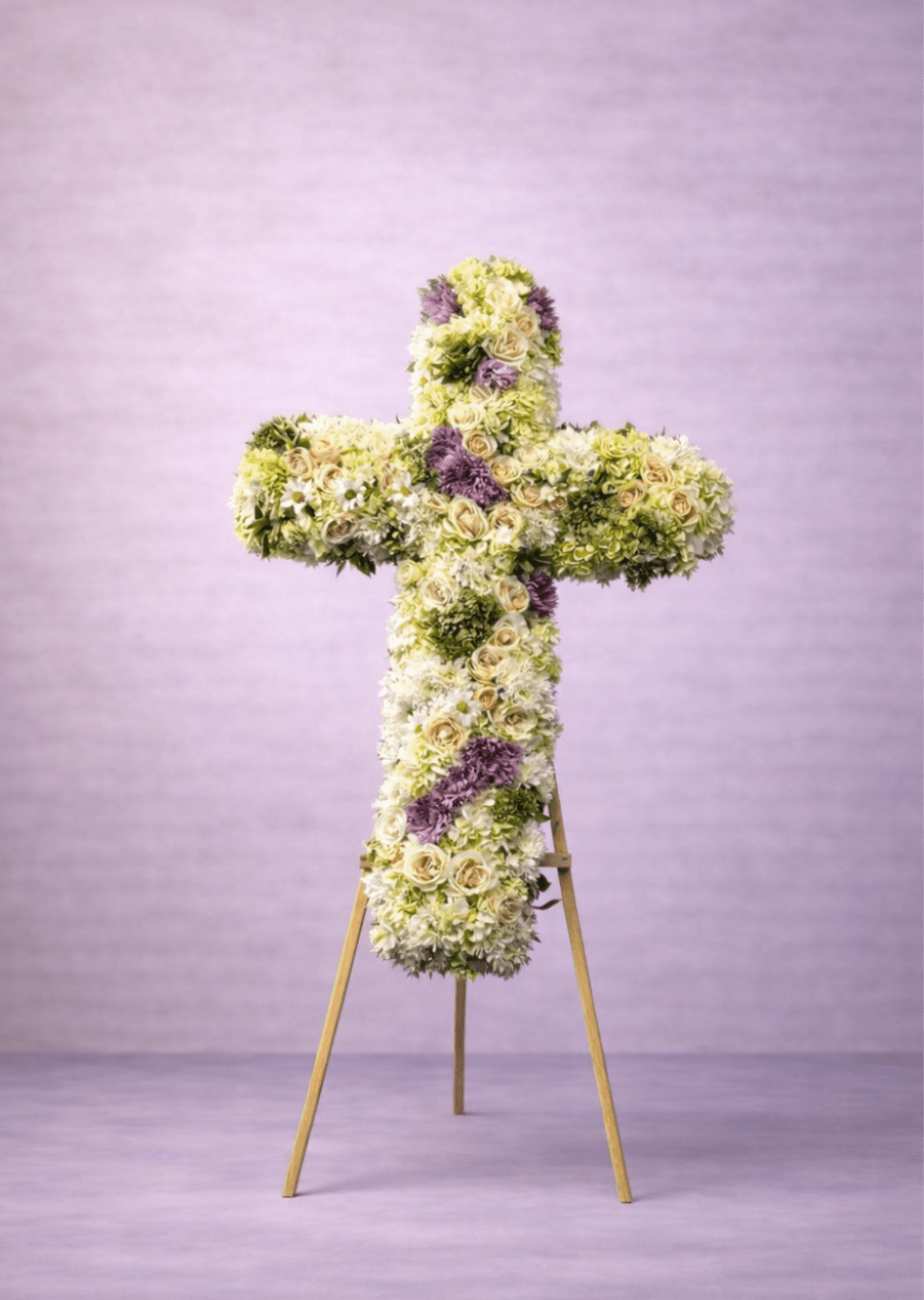 Tall floral cross of white and cream flowers with lavender accents on a wooden easel