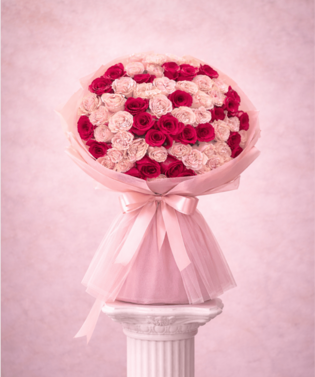 Large bouquet of pink and red roses wrapped in pale pink paper with a ribbon
