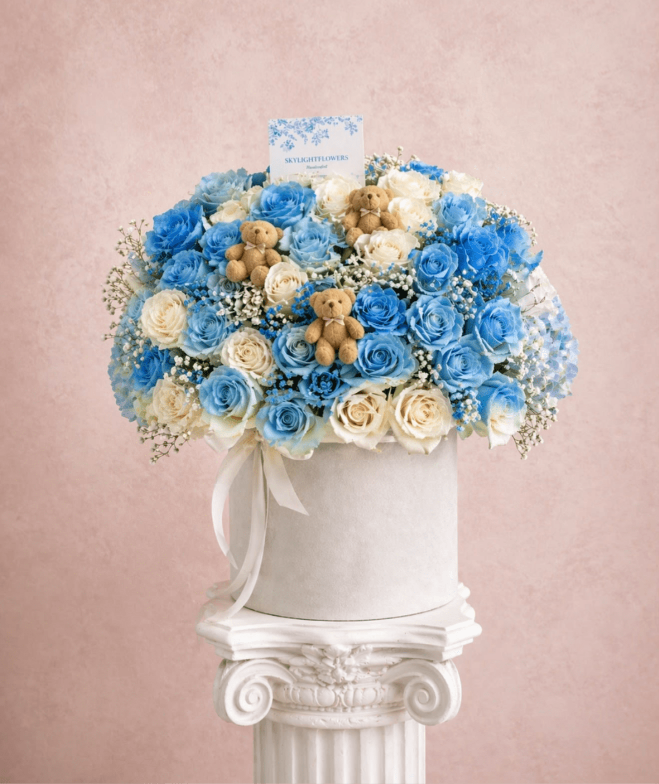 Blue and white rose arrangement in a white hat box with small teddy bears