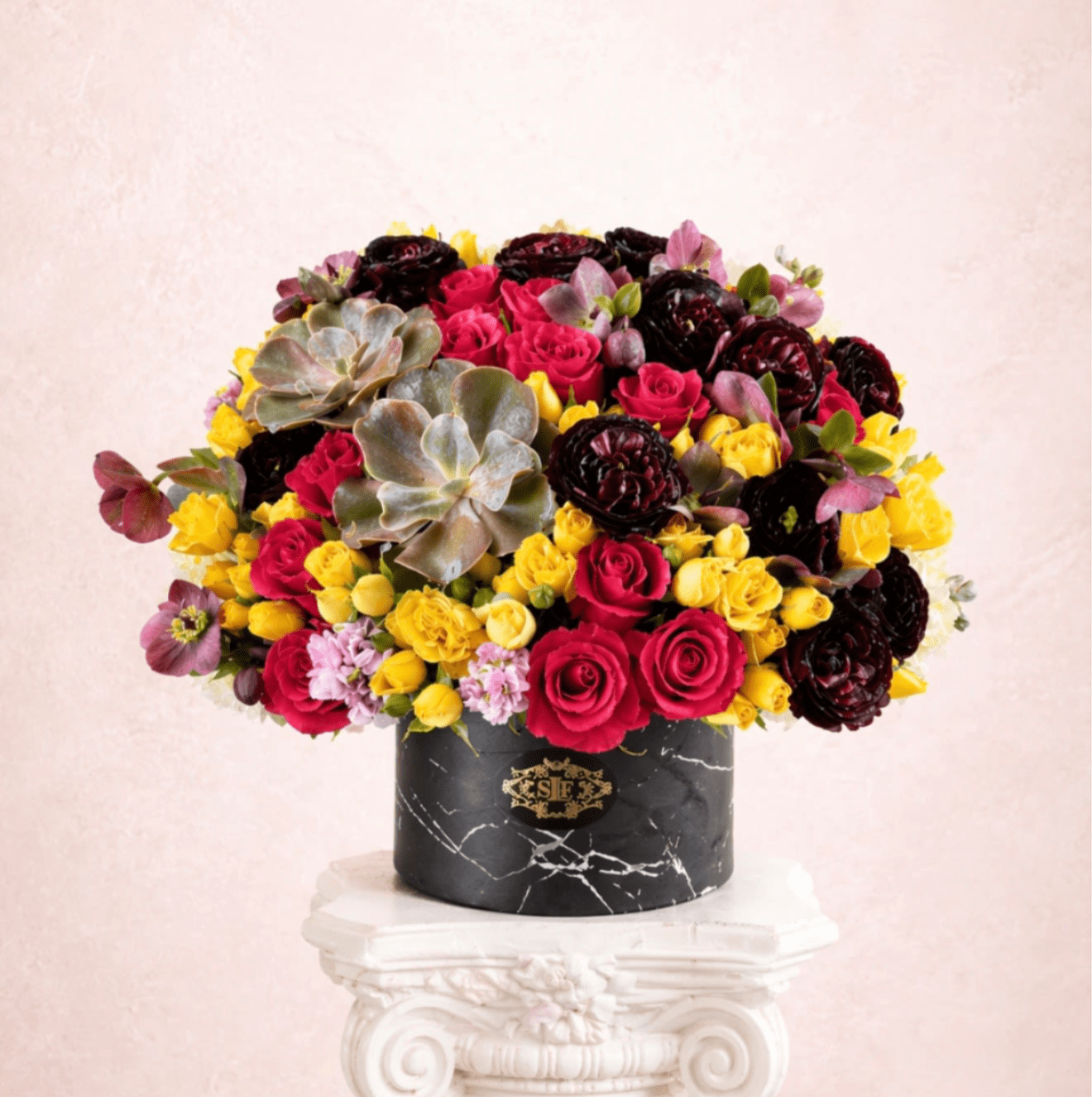 Mixed bouquet of pink, yellow, and dark red flowers in a black vase