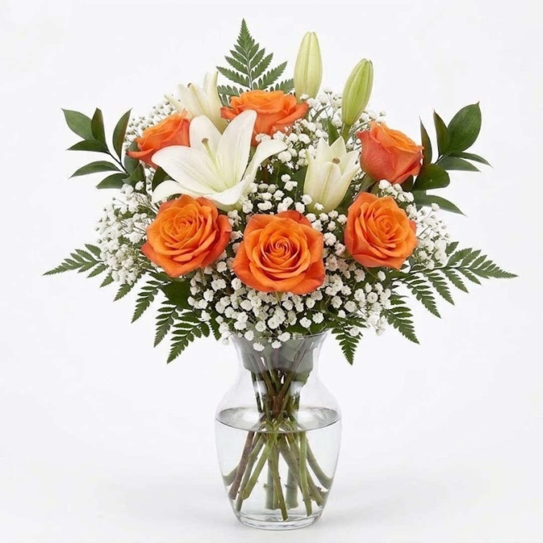 Orange roses and white lilies in a clear glass vase