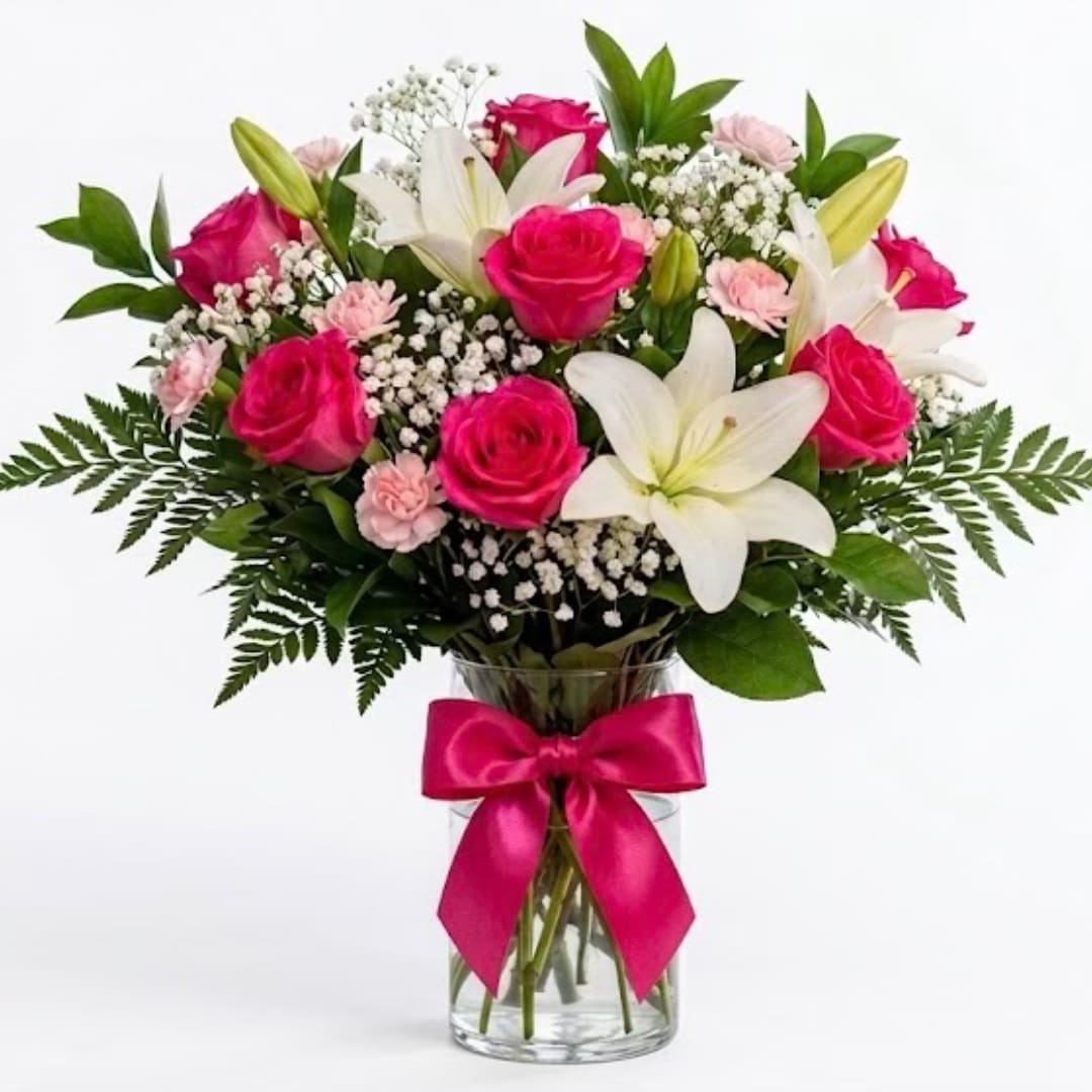Pink roses and white lilies in a glass vase with a pink ribbon