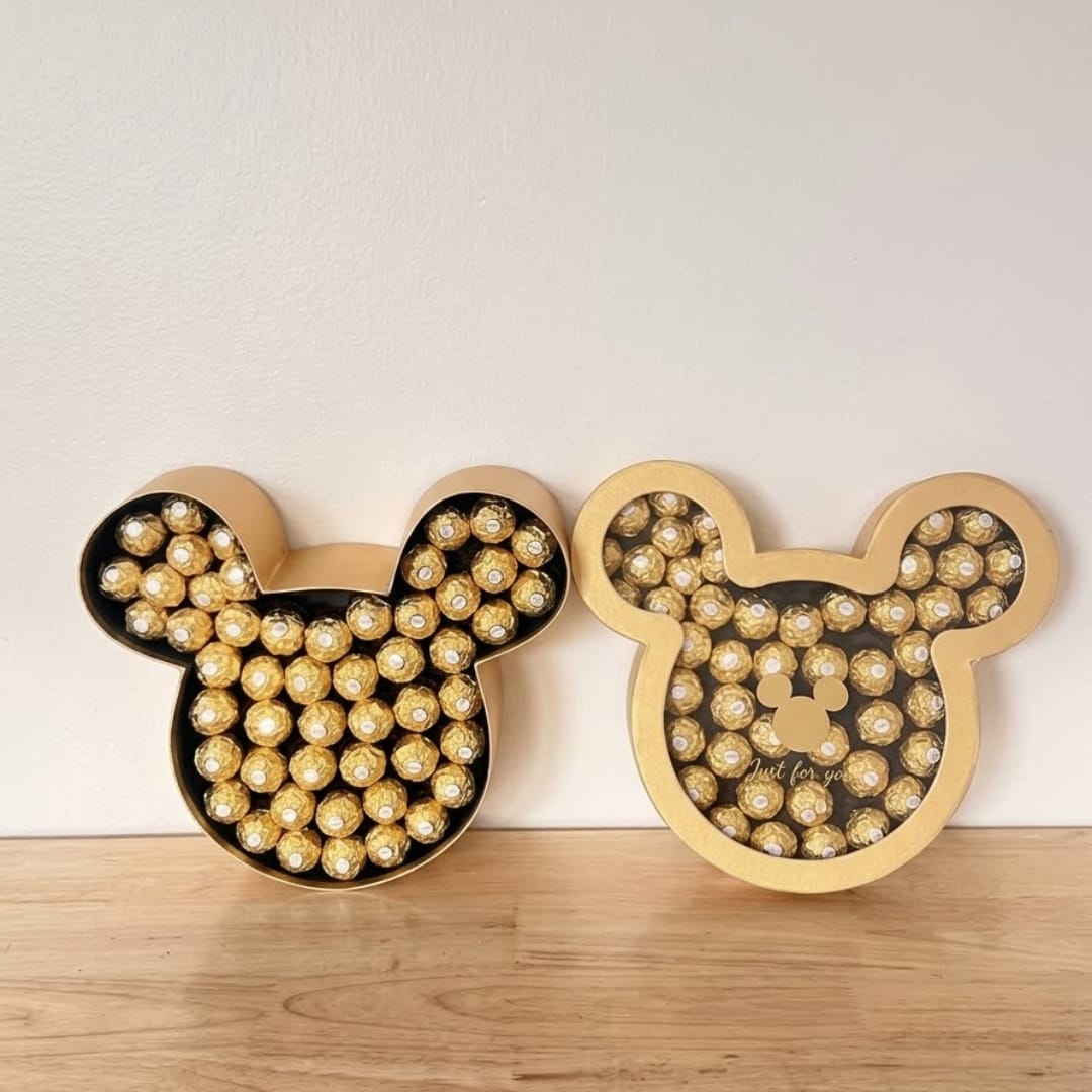 Two Mickey-shaped boxes filled with gold-wrapped chocolates on a wooden surface