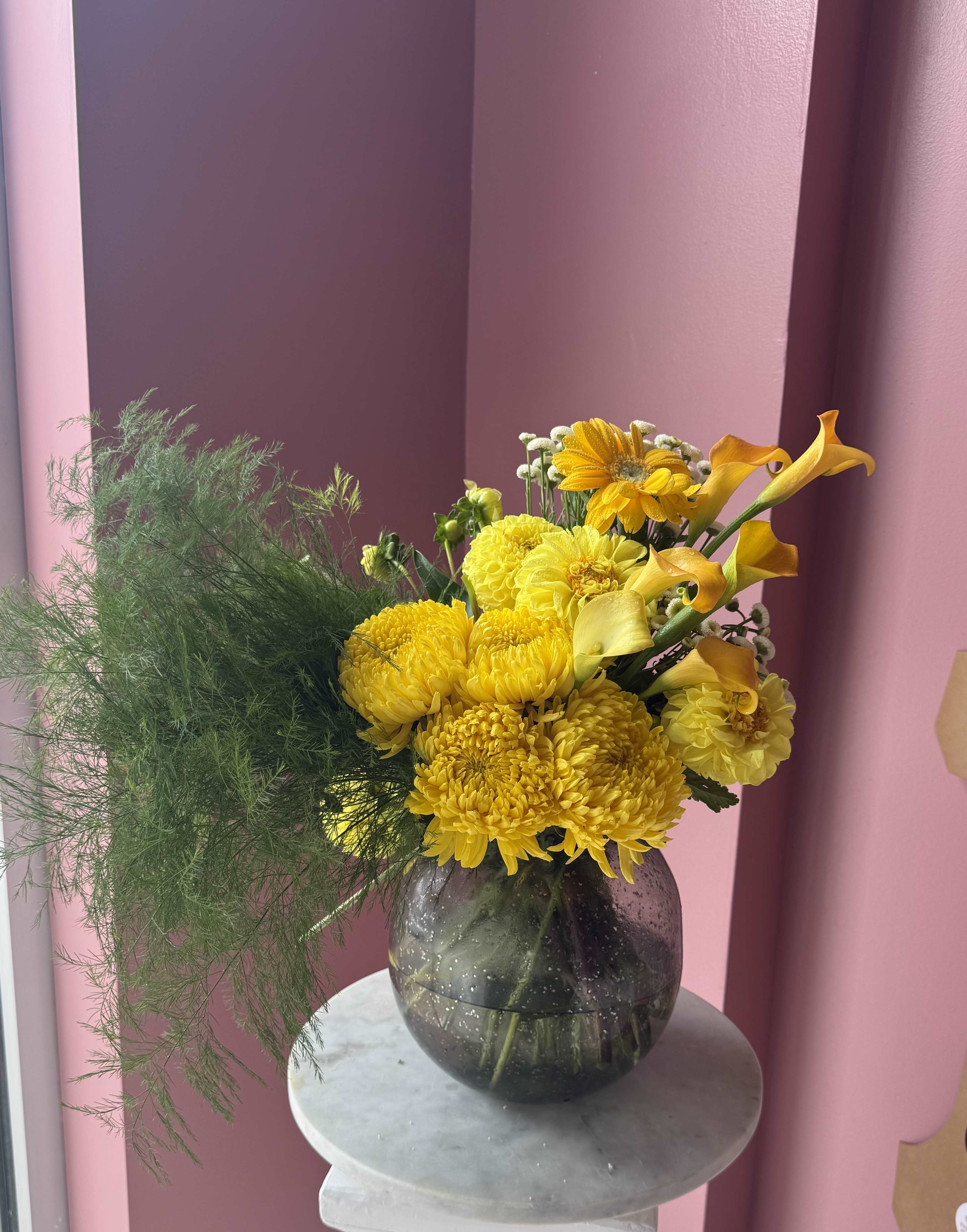 Yellow flowers in a dark glass vase with airy green foliage
