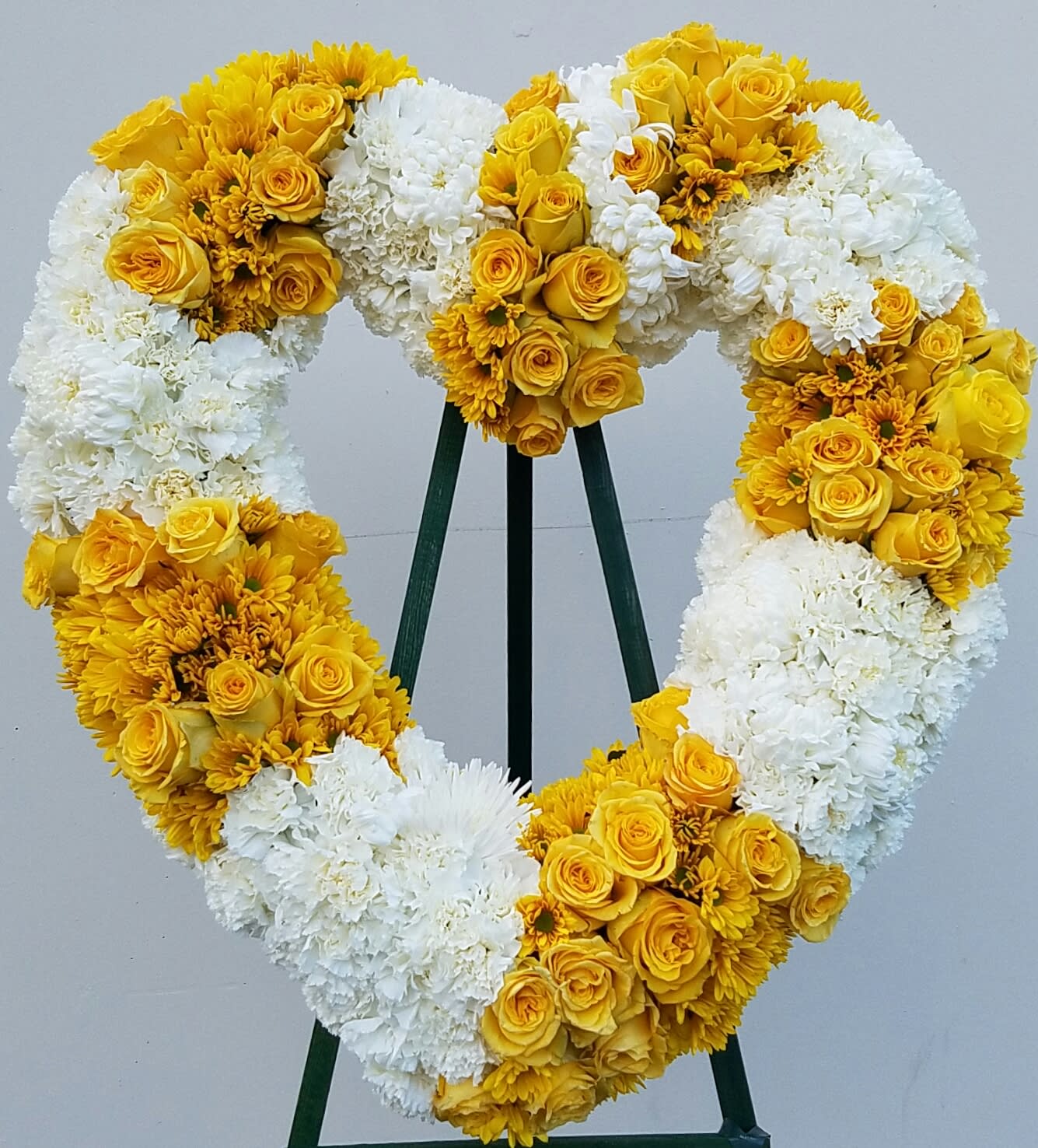 Heart-shaped floral wreath with yellow roses and white blooms on a stand