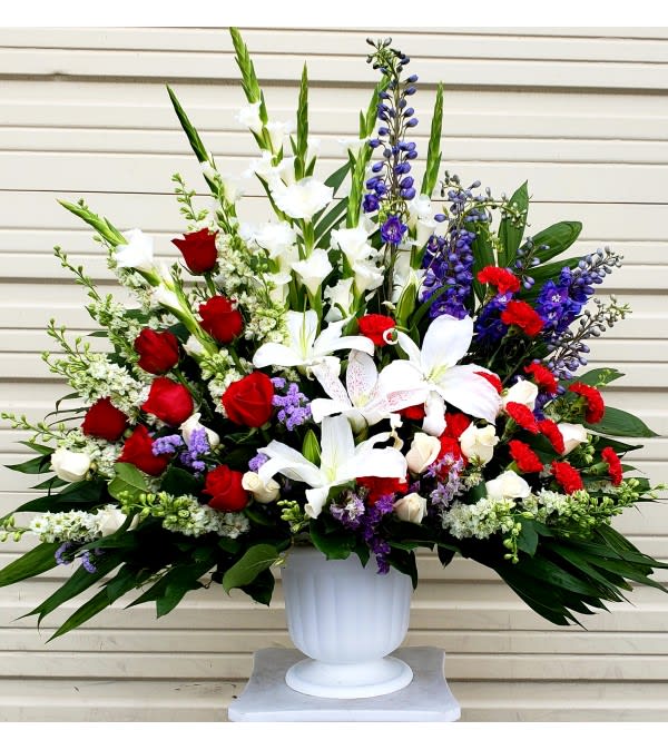 Large arrangement of red roses, white lilies, and purple flowers in a white urn