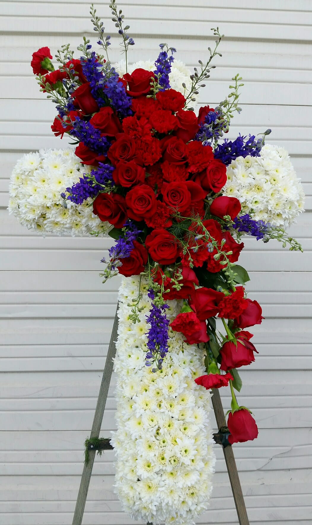 Standing floral cross with red roses, white chrysanthemums, and purple accents