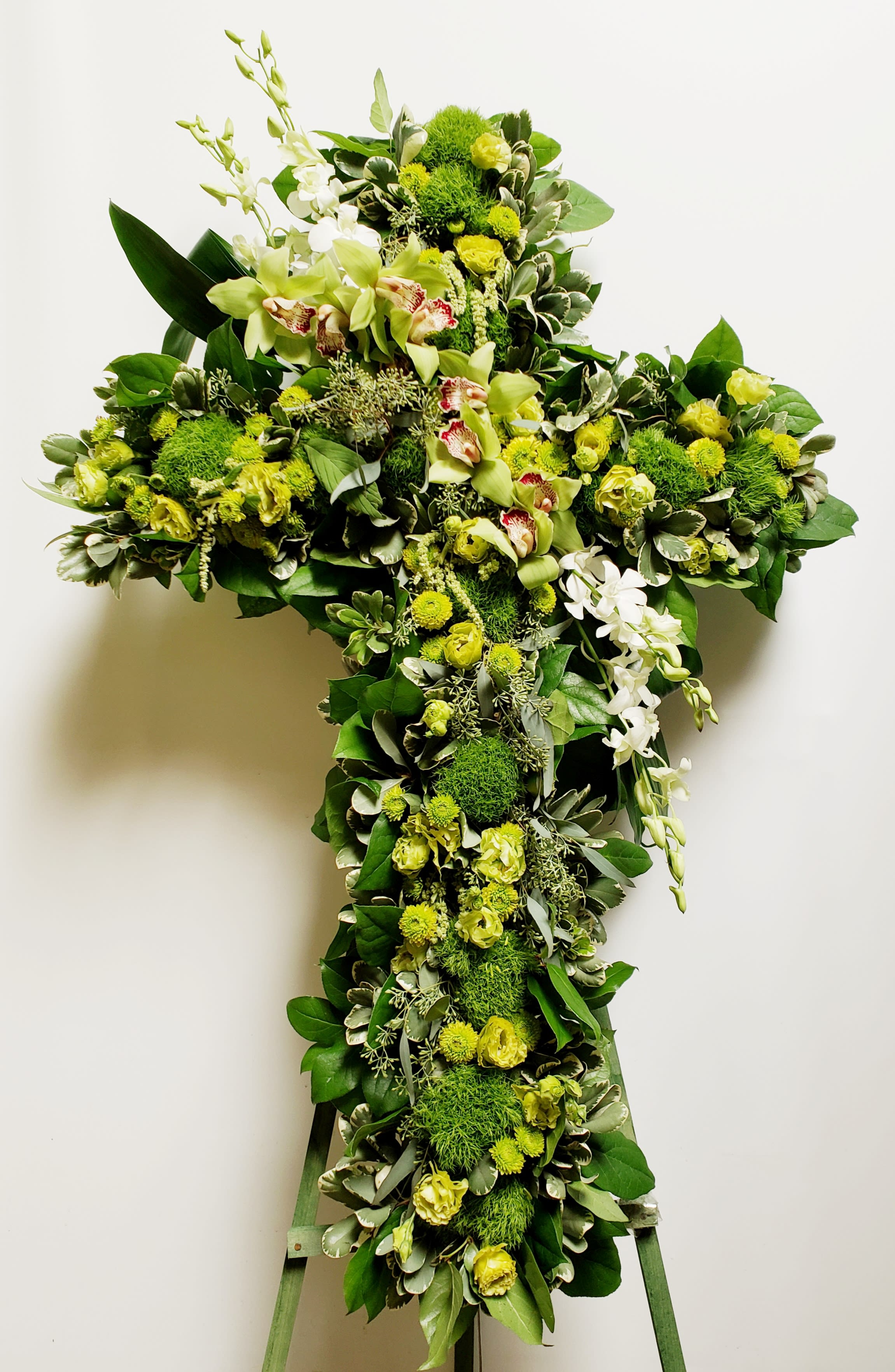 Green floral cross on an easel with white orchids and yellow blooms