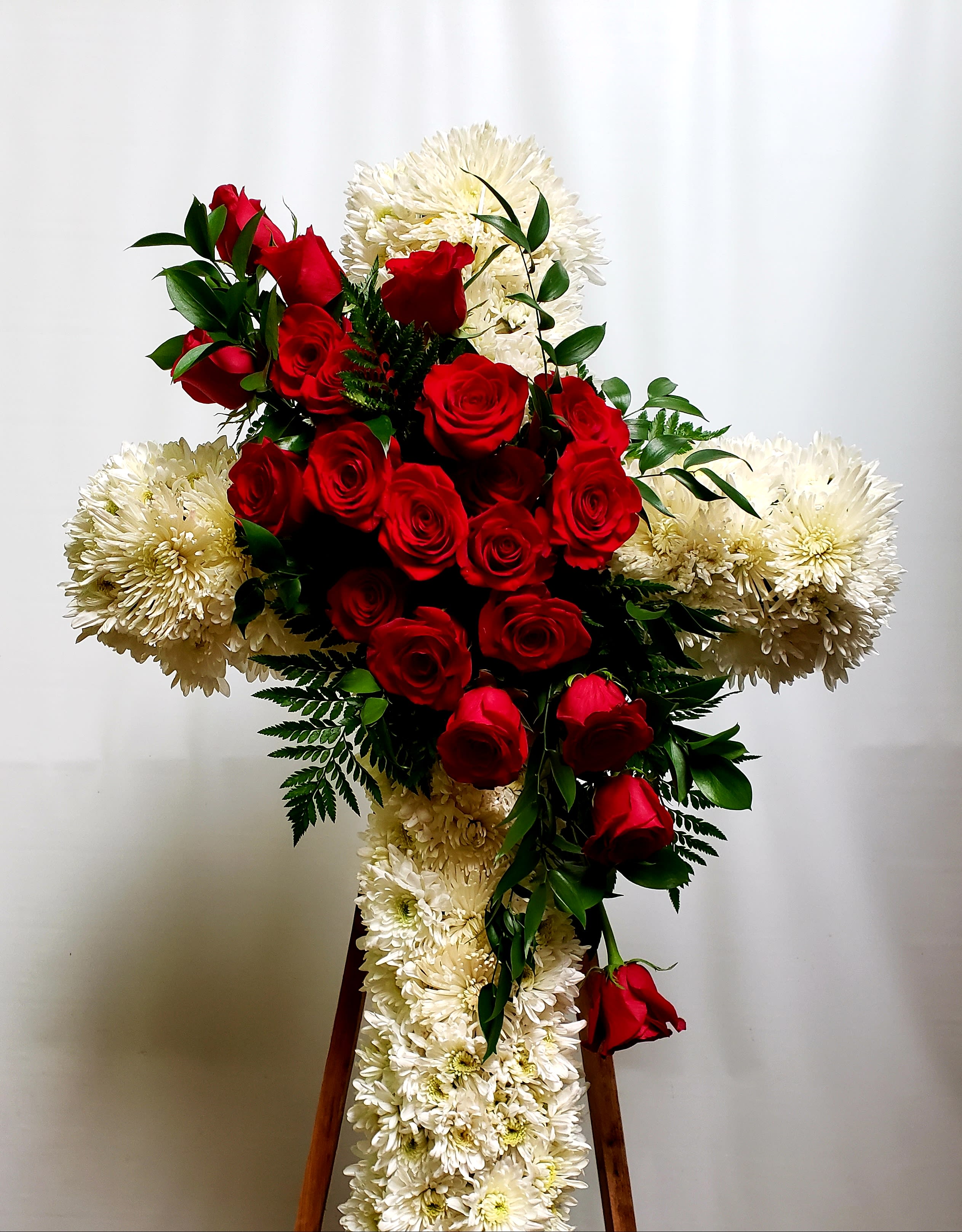 Red roses and white chrysanthemums arranged in a cross on a stand