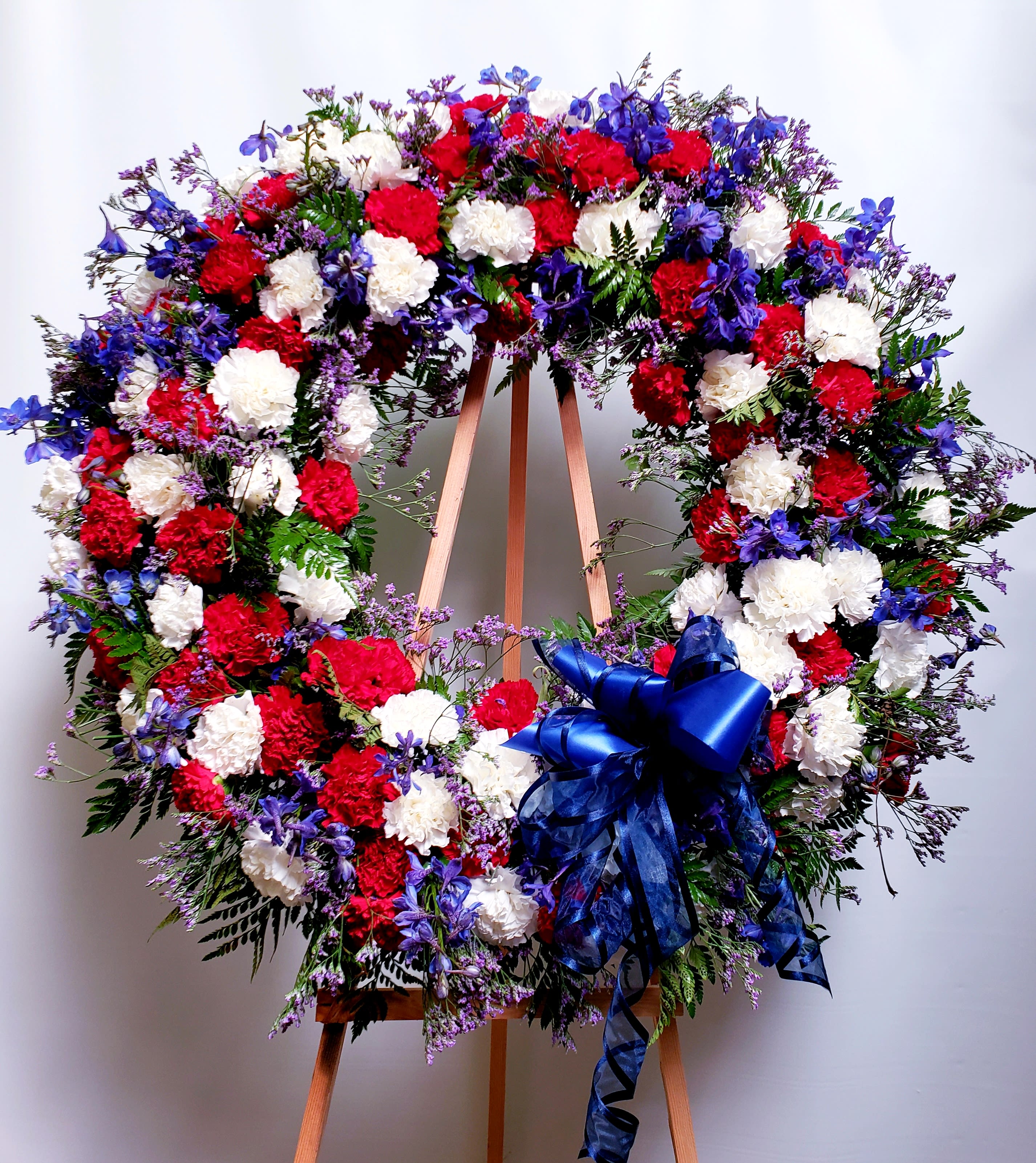 Large red, white, and blue floral wreath on an easel with a ribbon bow