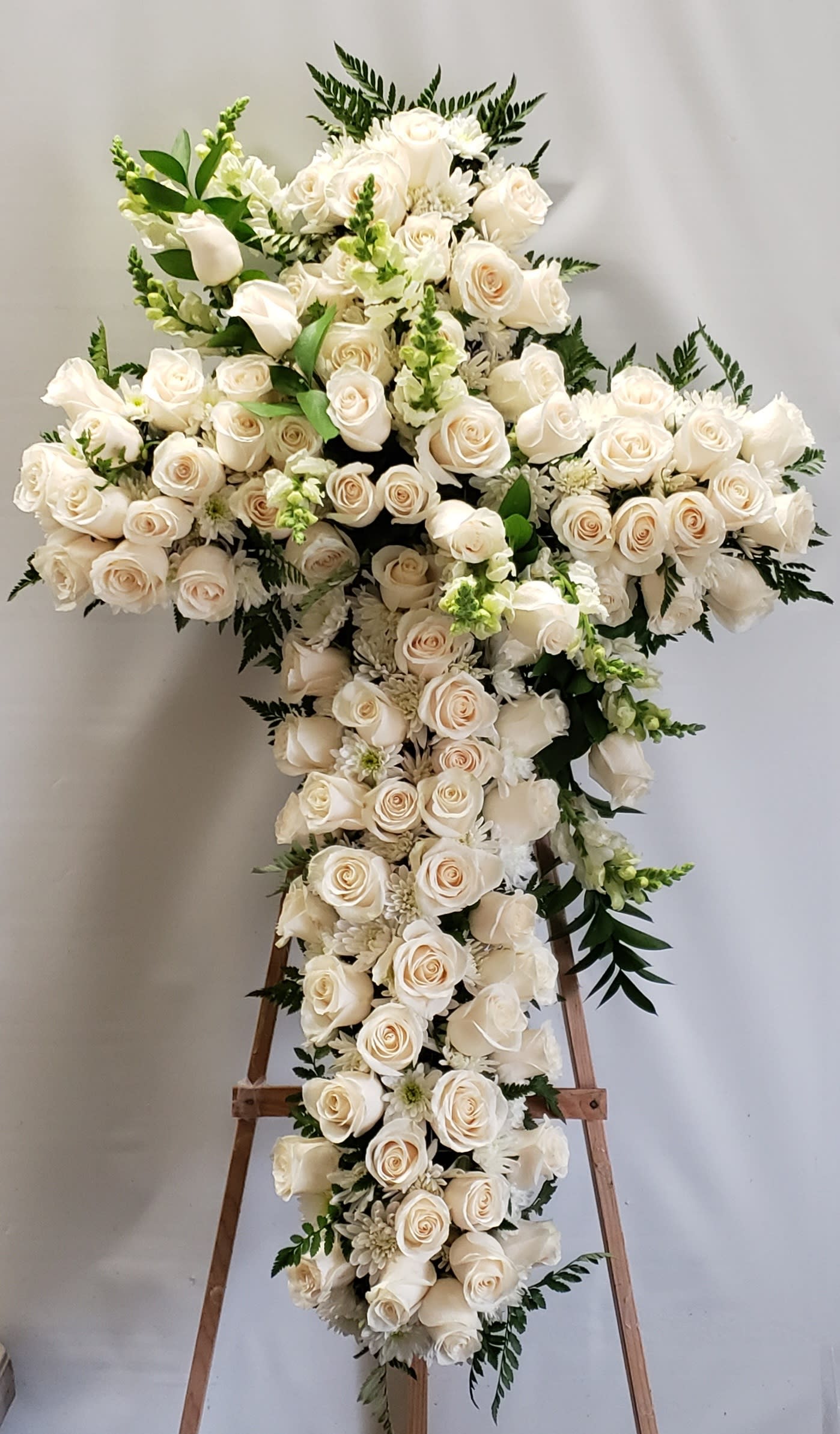 Large white rose cross arrangement on a wooden stand