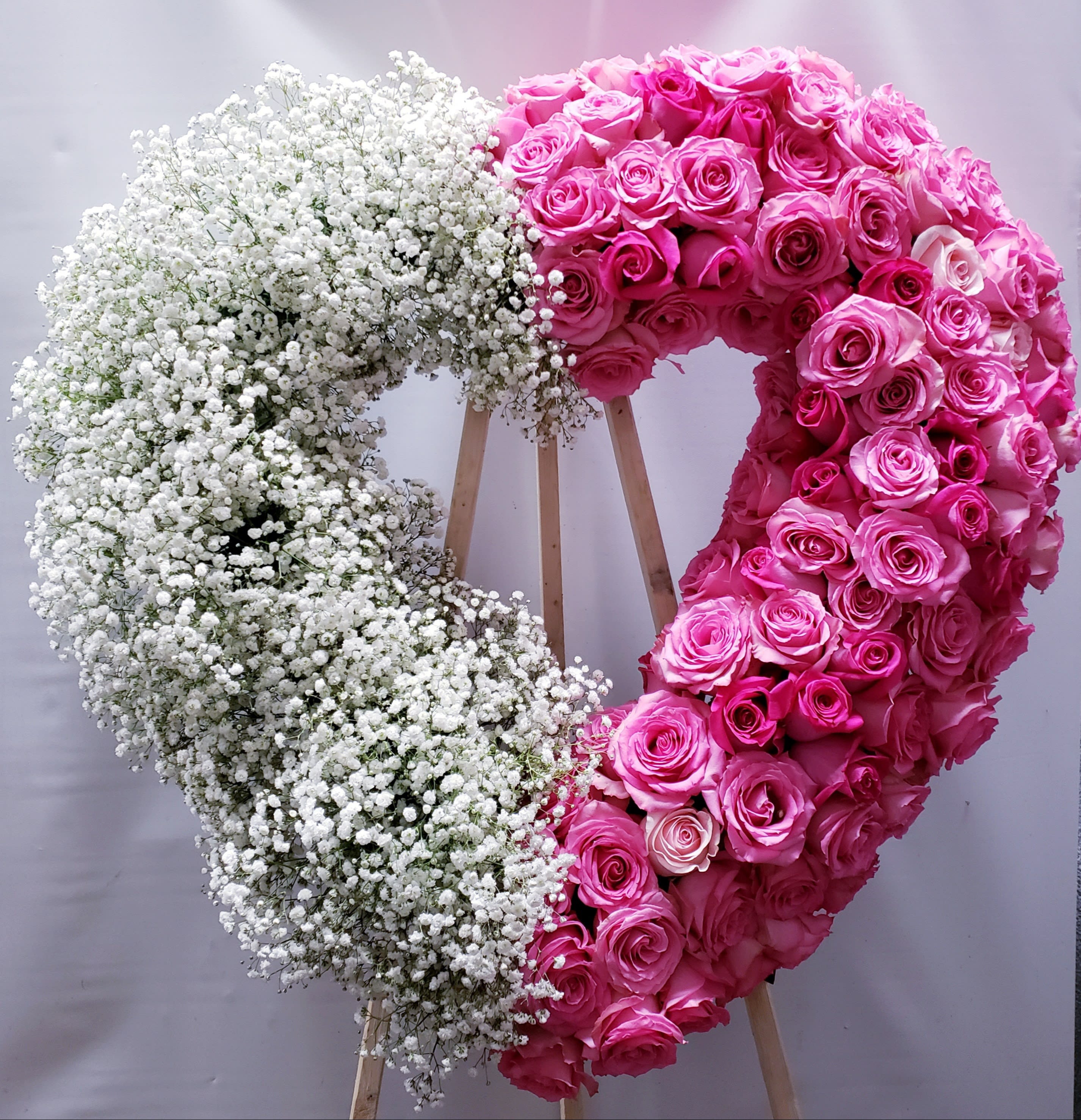 Heart-shaped floral wreath with pink roses and white baby's breath on a stand