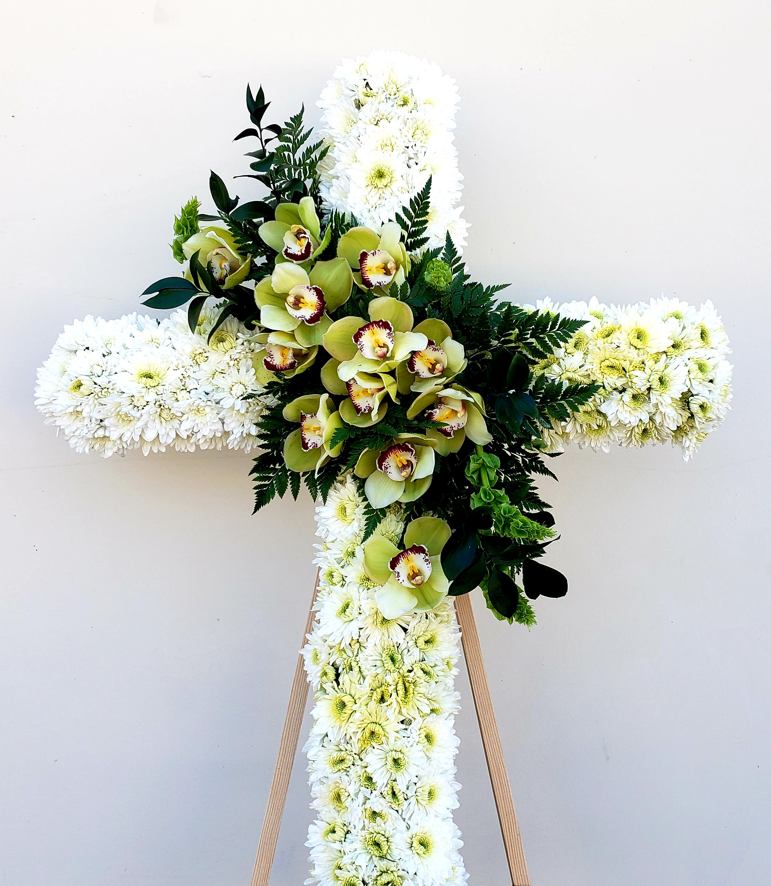 White floral cross with green orchids and dark foliage on an easel