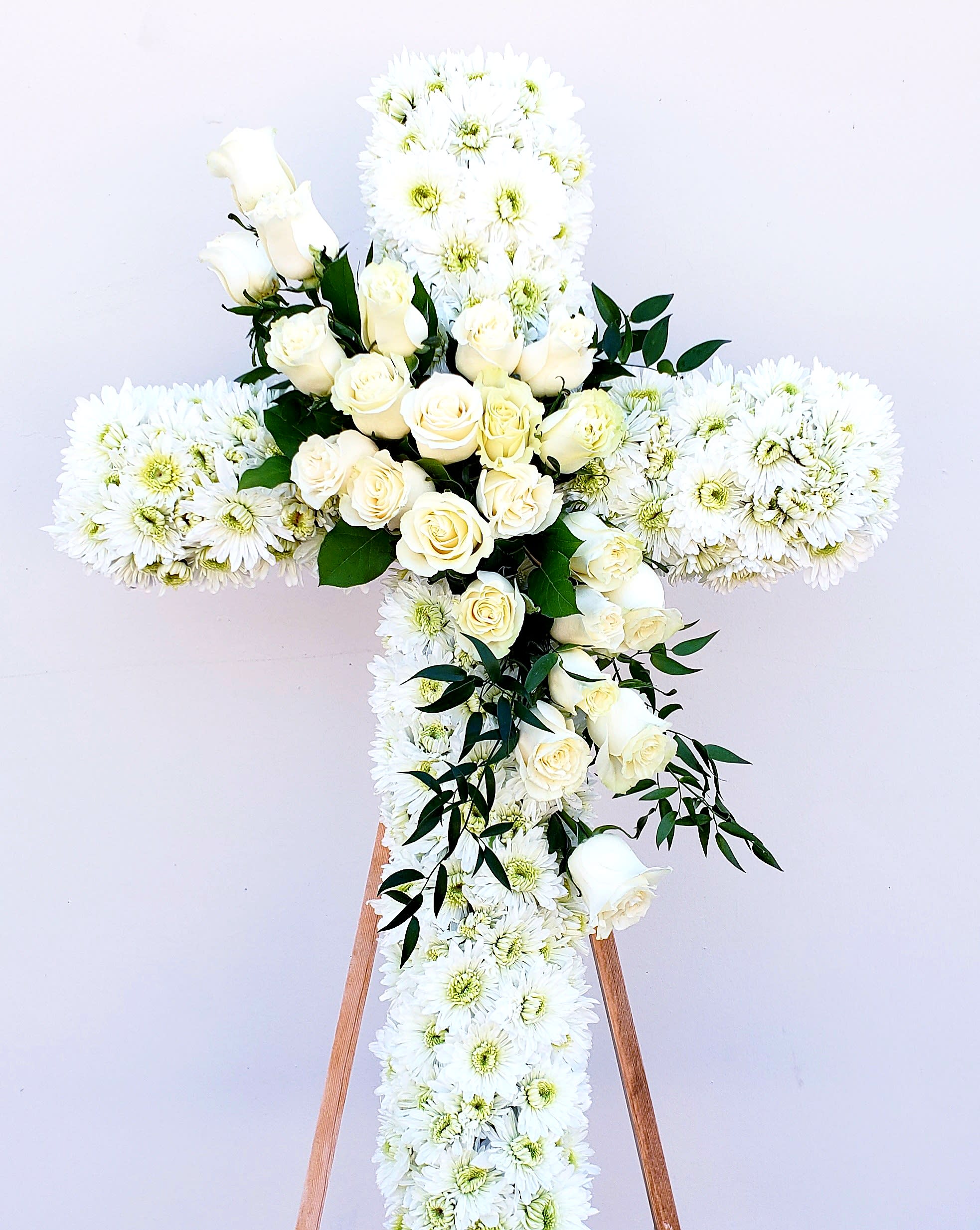 White floral cross with roses and daisies on a stand