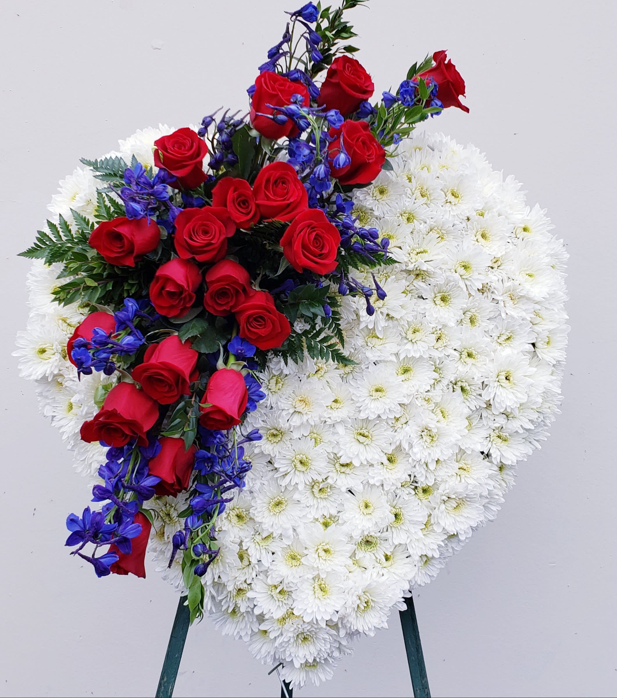 Heart-shaped floral spray with red roses, white daisies, and blue flowers