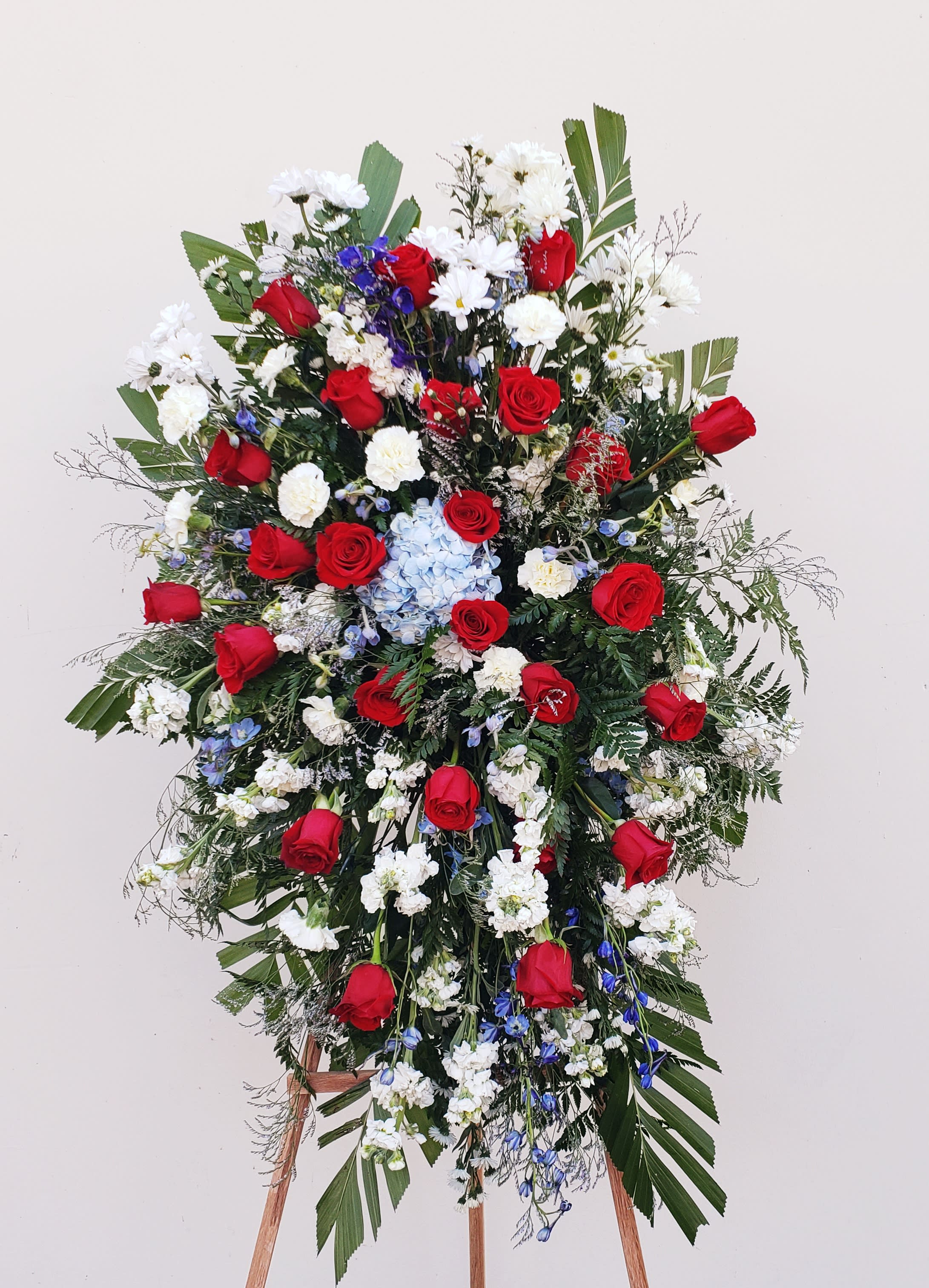 Large standing floral spray with red roses, white blooms, and blue accents