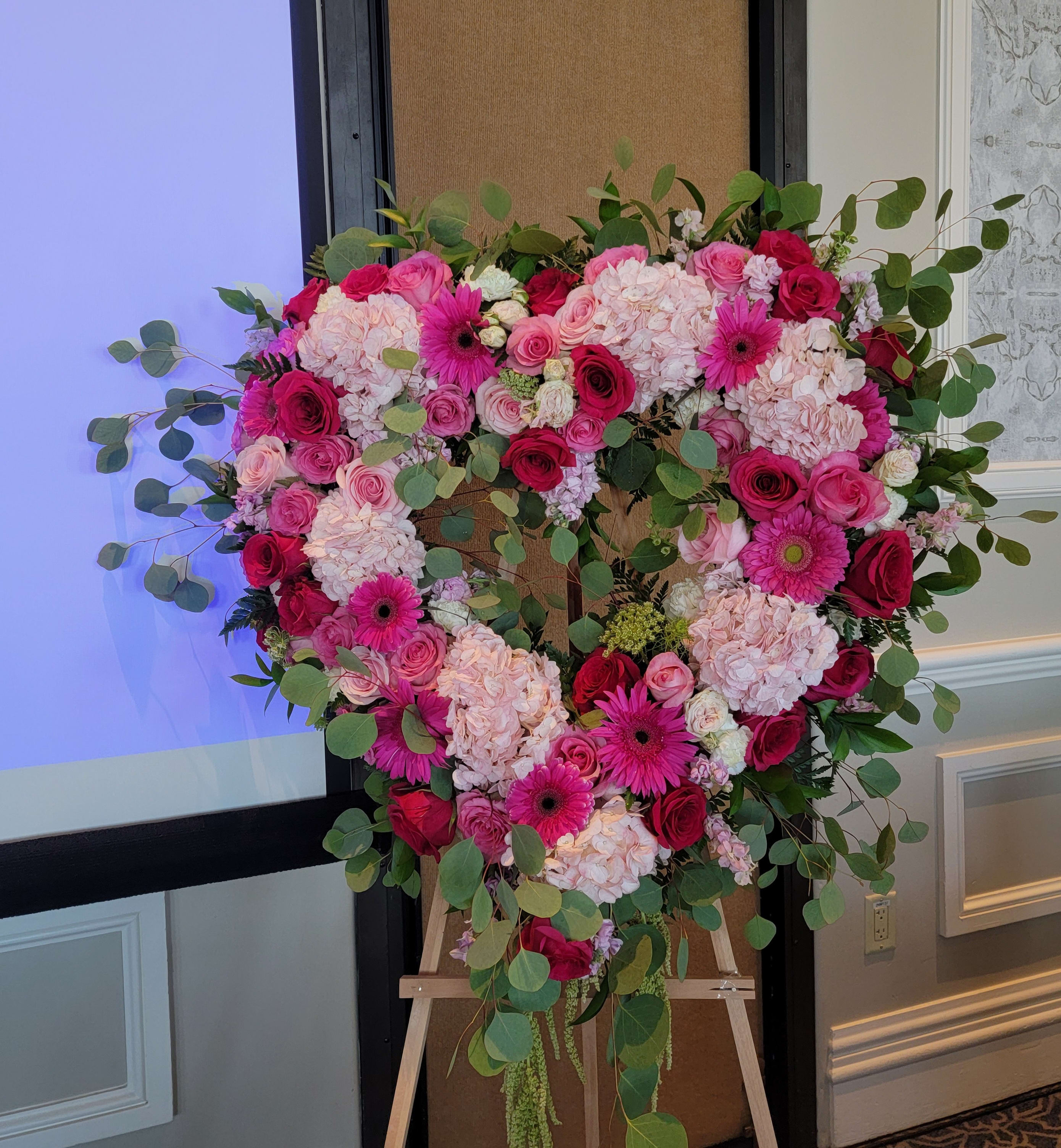 Heart-shaped floral arrangement with pink roses, hydrangeas, and gerbera daisies on an easel