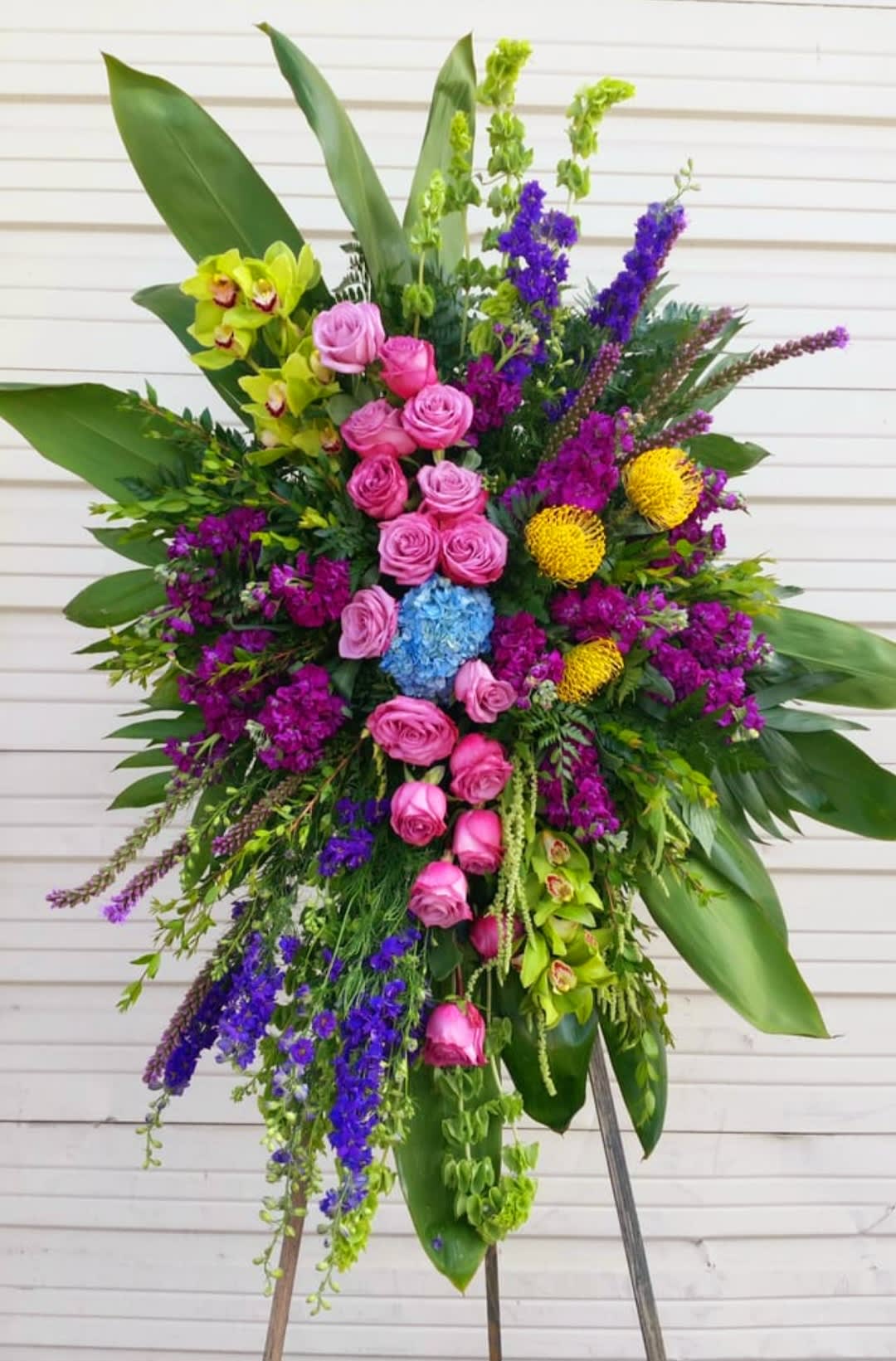 Large standing floral spray with pink roses, purple blooms, and green orchids