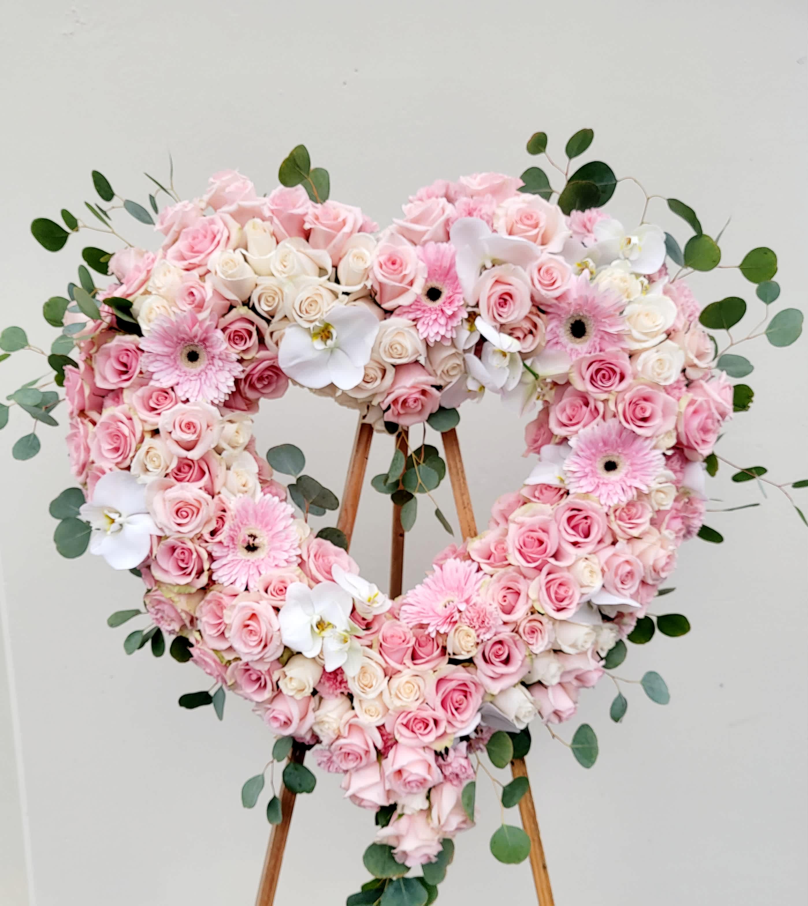 Heart-shaped floral arrangement of pink and white roses with orchids and daisies