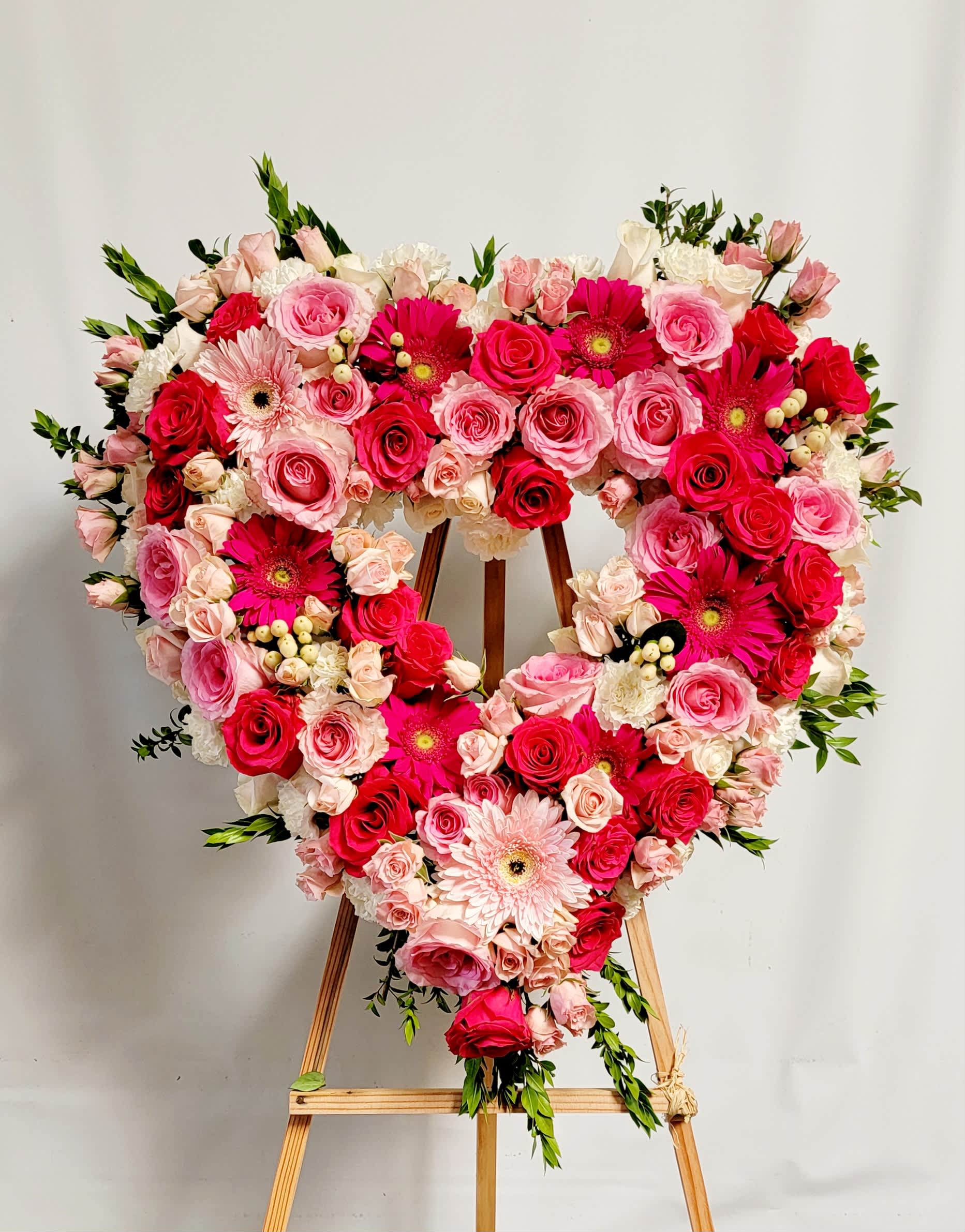 Heart-shaped floral wreath of pink and red roses with gerbera daisies on an easel