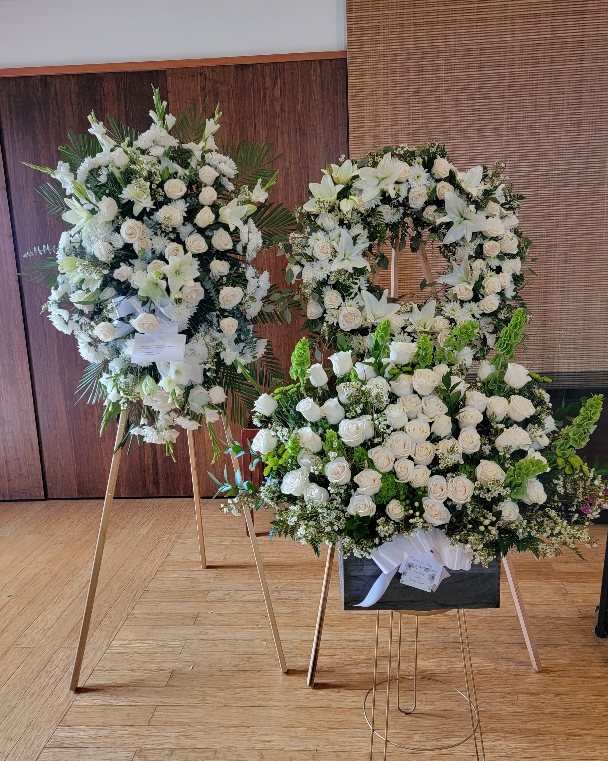 White floral funeral wreaths on stands with roses and lilies