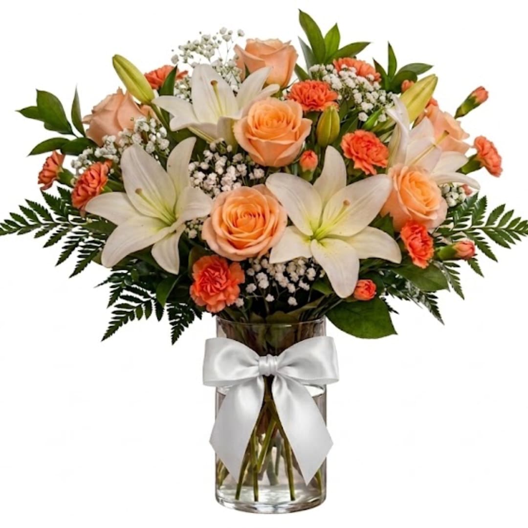 Peach roses and white lilies in a glass vase with a white ribbon