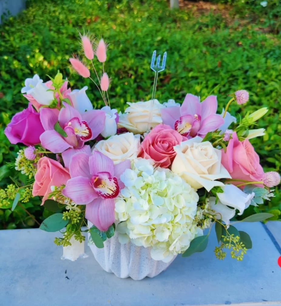 Pink and white floral arrangement in a white vase with orchids and roses