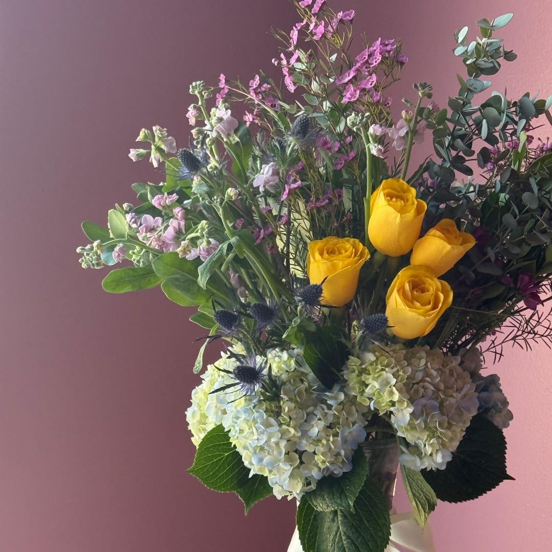 Bouquet of yellow roses, white hydrangeas, and purple flowers in a vase