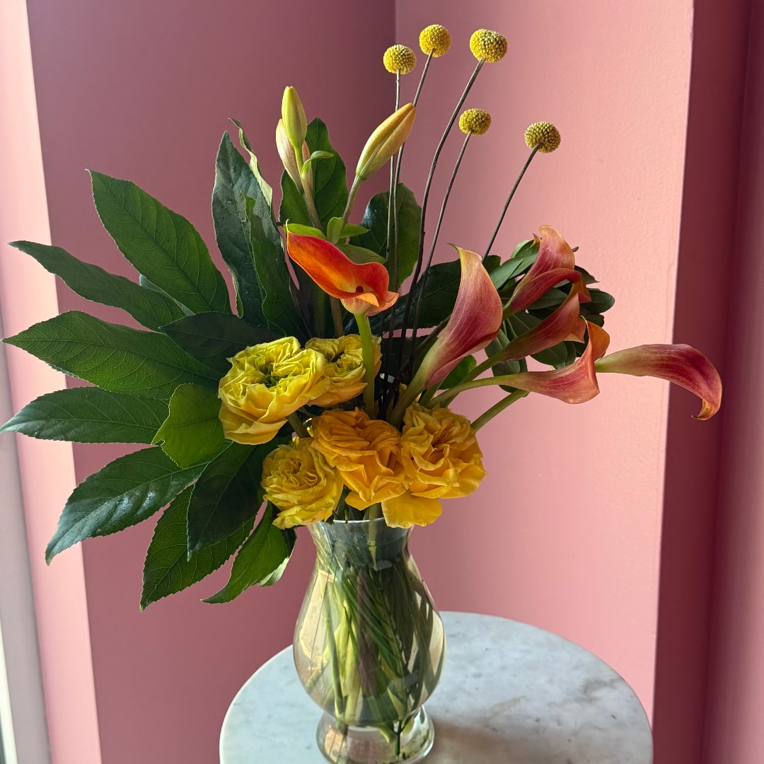 Yellow roses and orange calla lilies in a clear glass vase