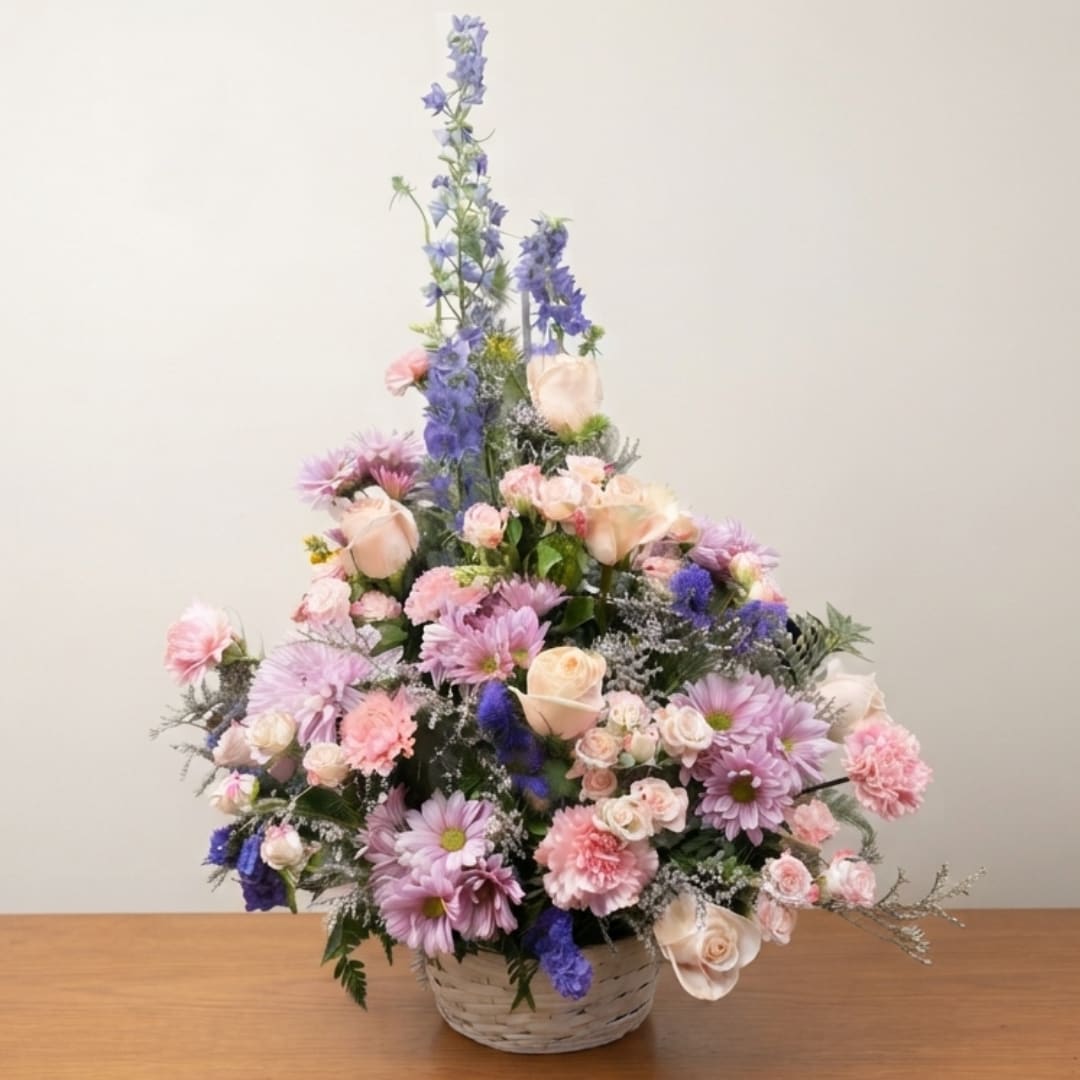 Pastel floral arrangement in a woven basket with tall blue blooms and pink flowers