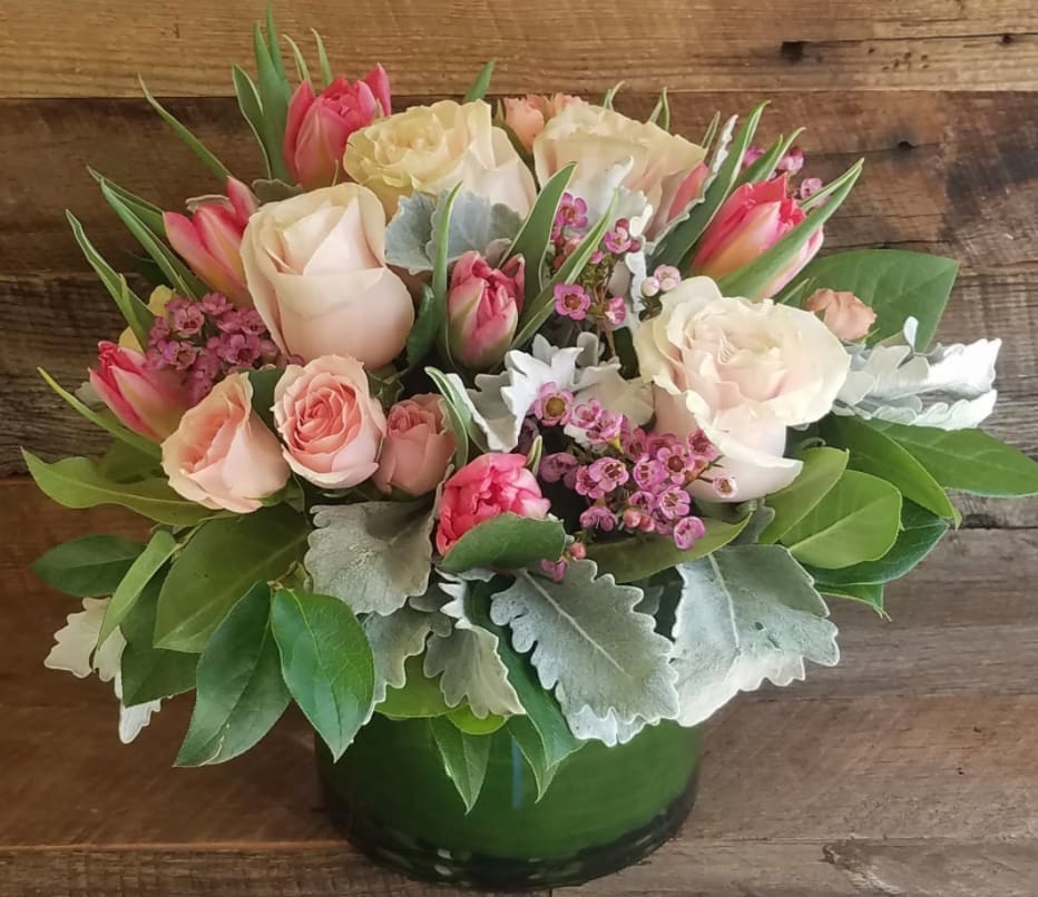 Low arrangement of pink and cream roses and tulips in a green vase with small pink filler blooms