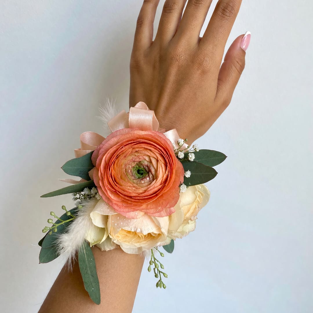 Peach and cream wrist corsage with ribbon and greenery on a hand