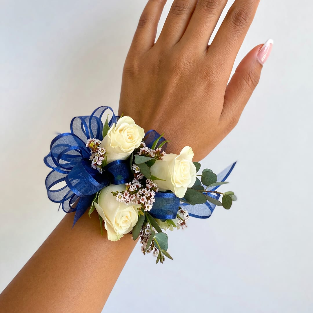 White rose wrist corsage with blue ribbon and small filler flowers