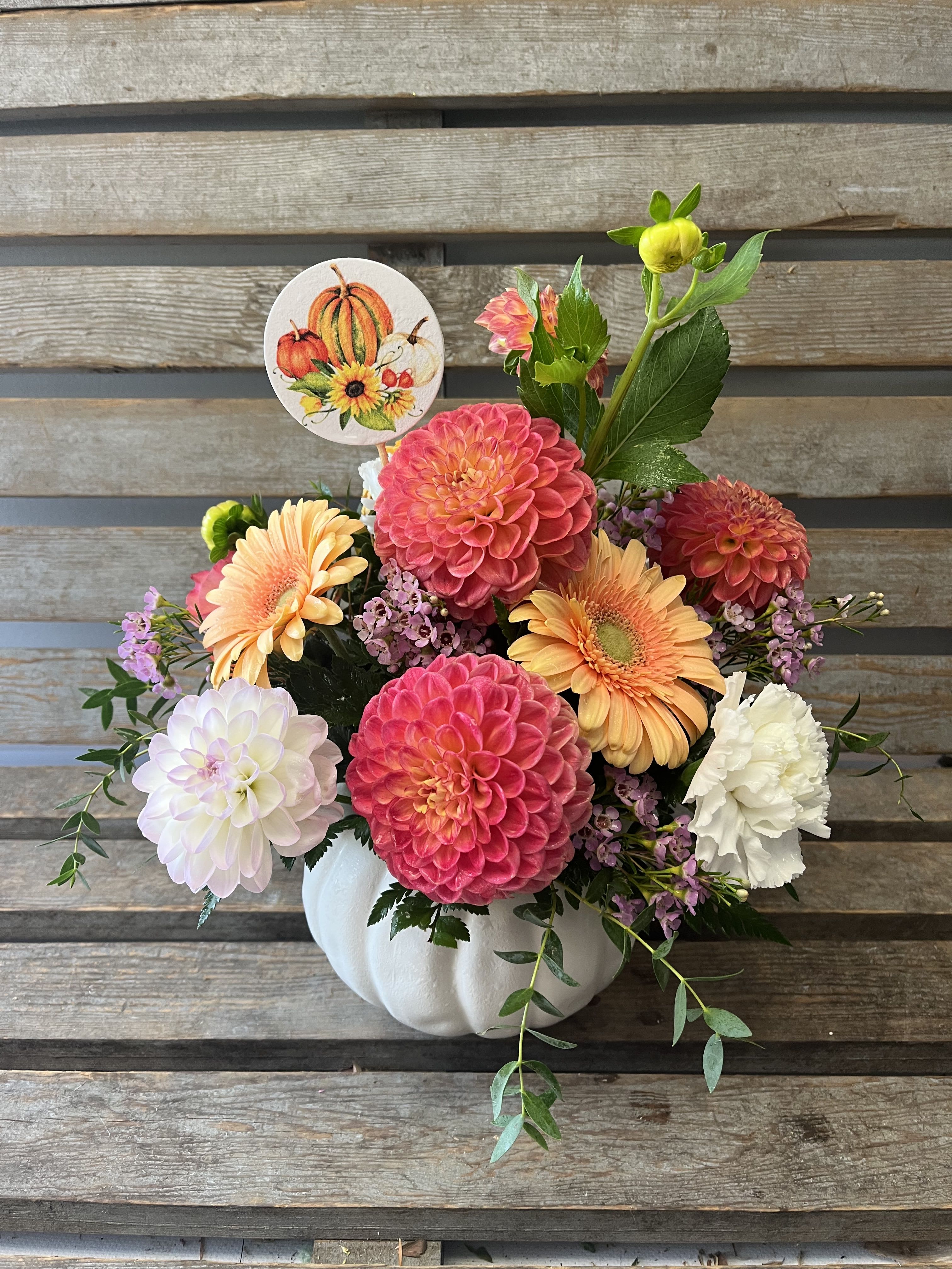 Fall floral arrangement in a white pumpkin container with colorful blooms and a pumpkin pick