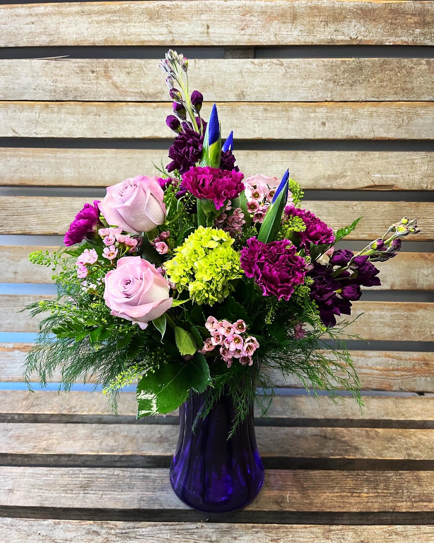 Mixed bouquet of pink roses, purple blooms, and green hydrangea in a purple vase