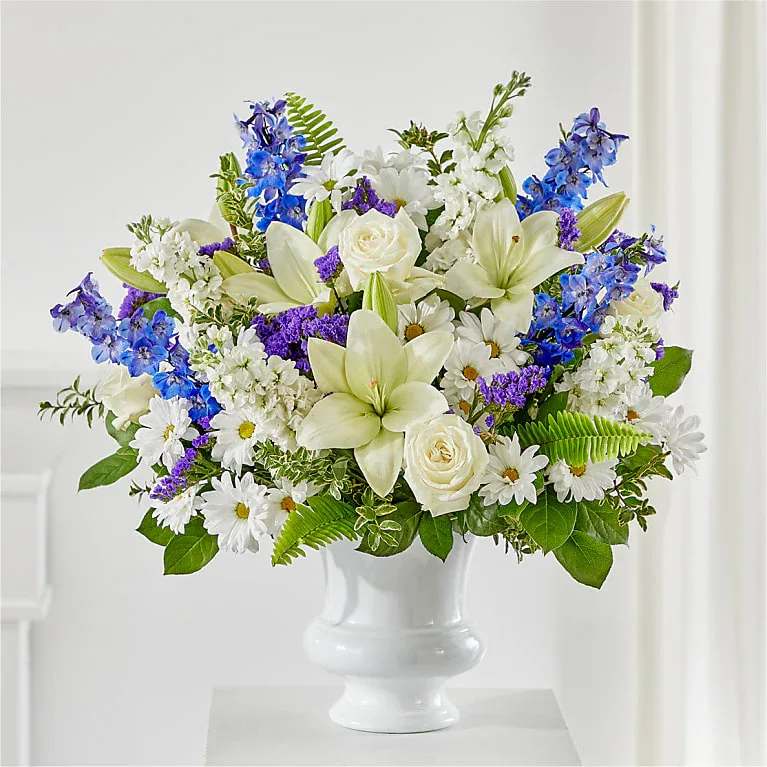White lilies, roses, daisies, and blue flowers in a white vase
