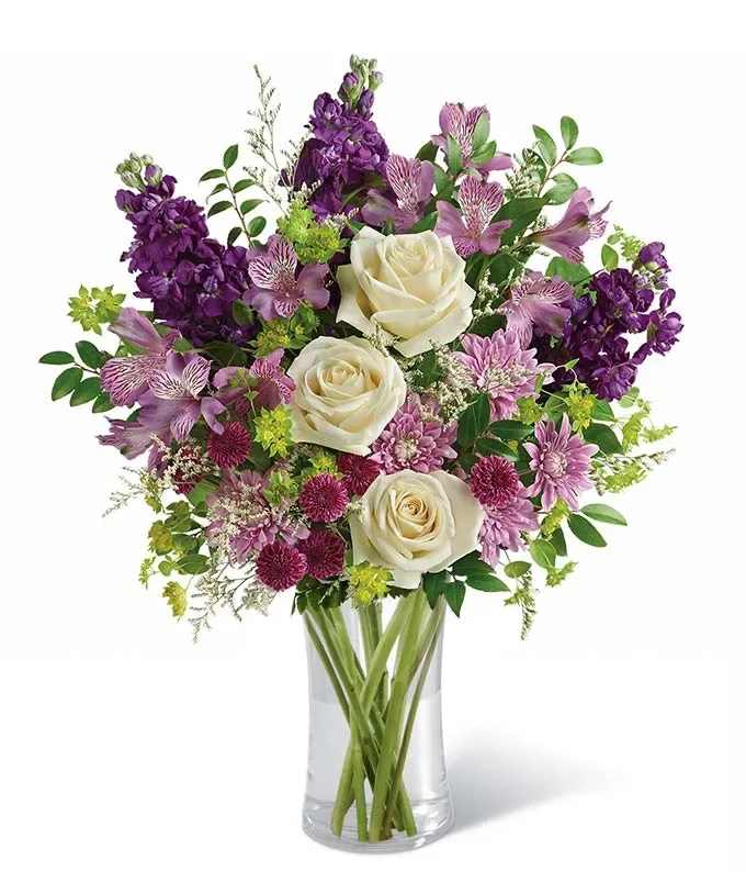 Bouquet of white roses and purple flowers in a clear glass vase