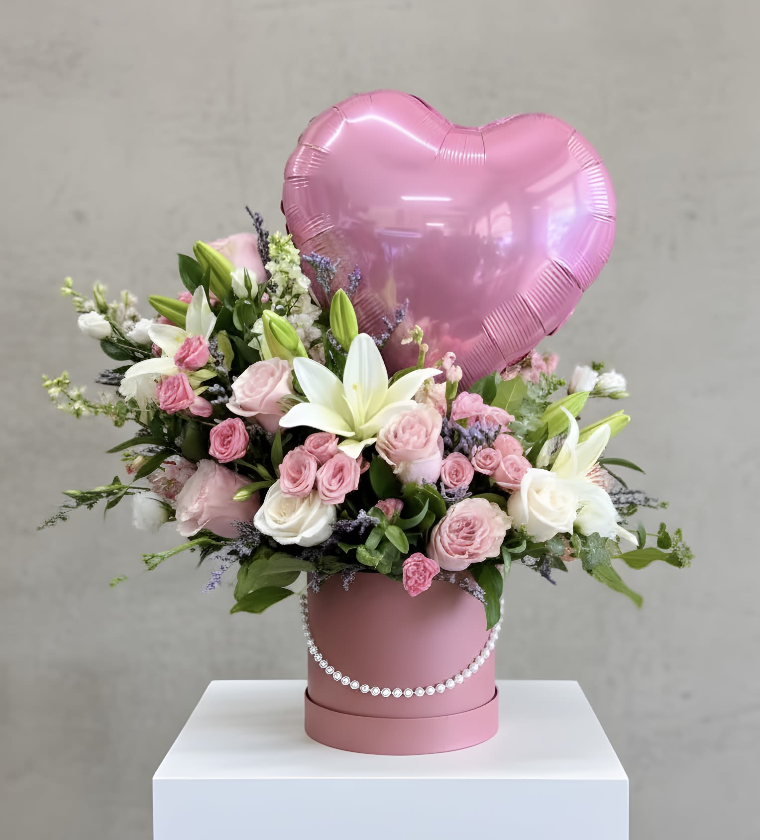 Pink heart balloon above a pink flower box with roses and lilies