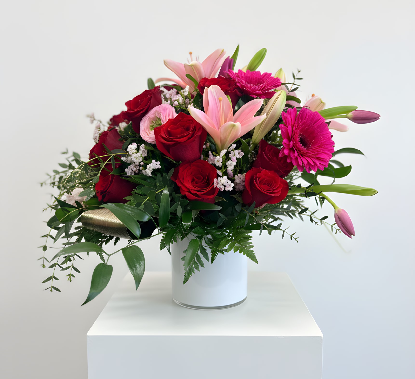 Bouquet of red roses, pink lilies, and magenta gerbera daisies in a white vase