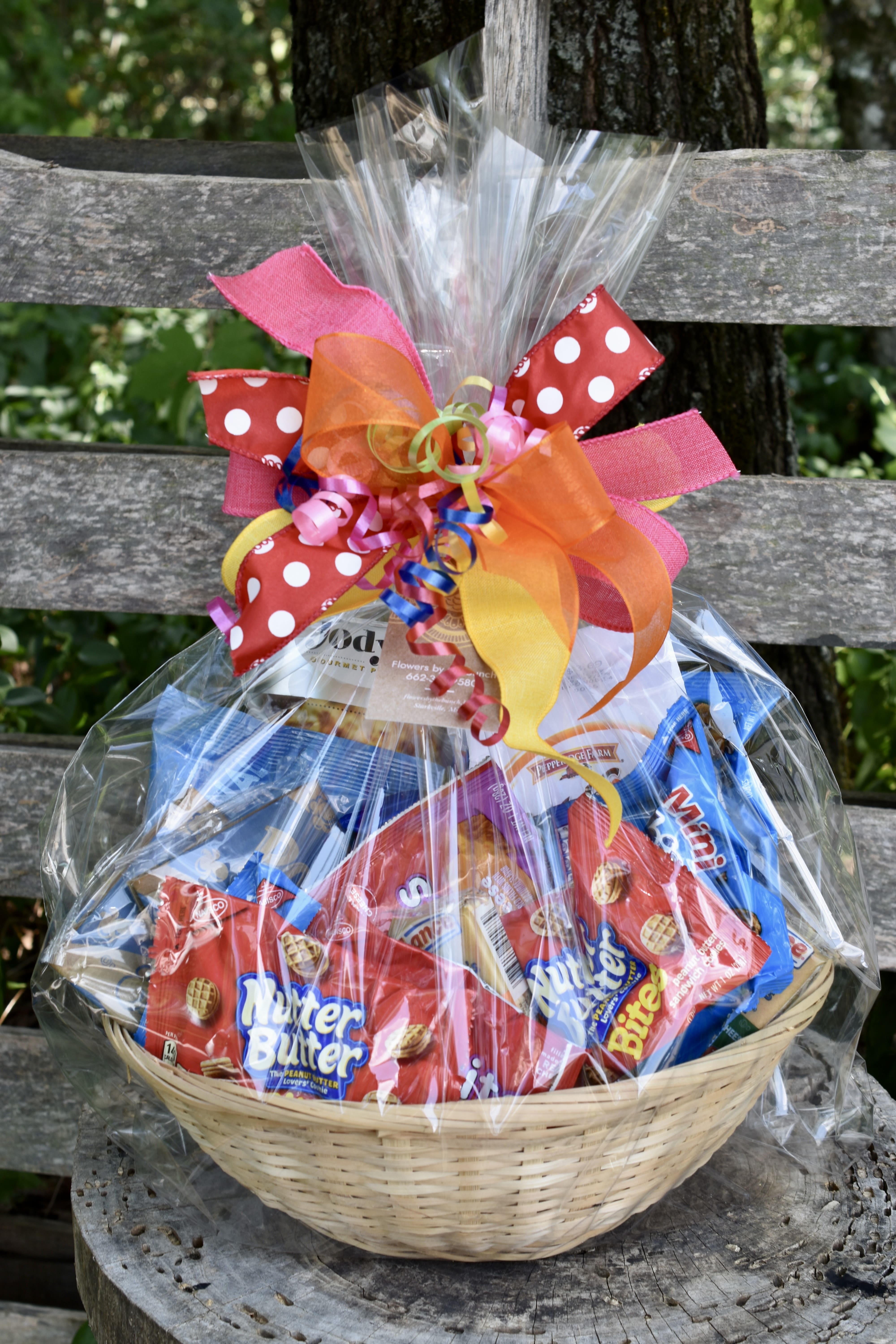 Basket of assorted snack packs wrapped in clear cellophane with colorful ribbon