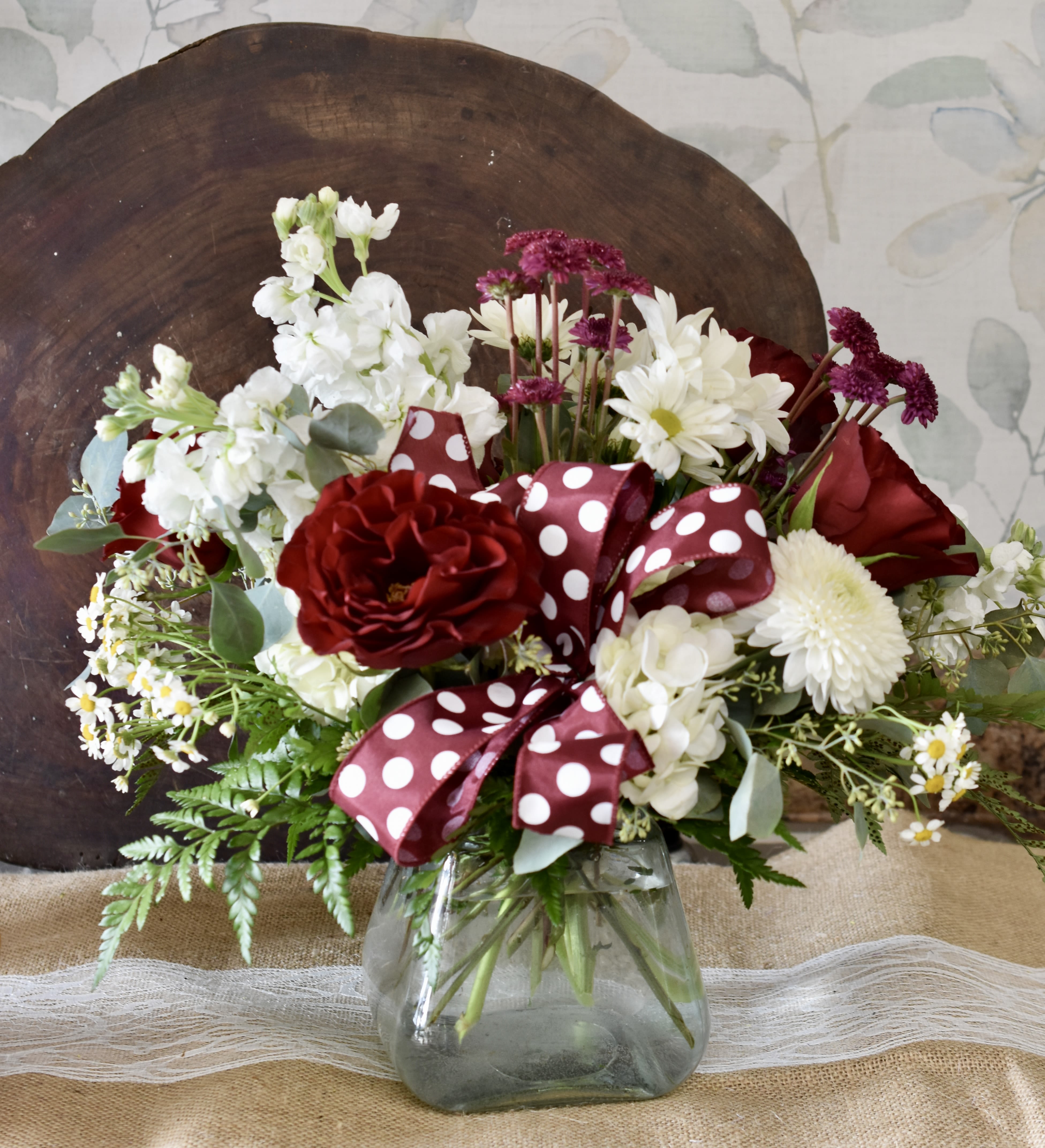 Red and white flower arrangement in a glass vase with a polka-dot ribbon