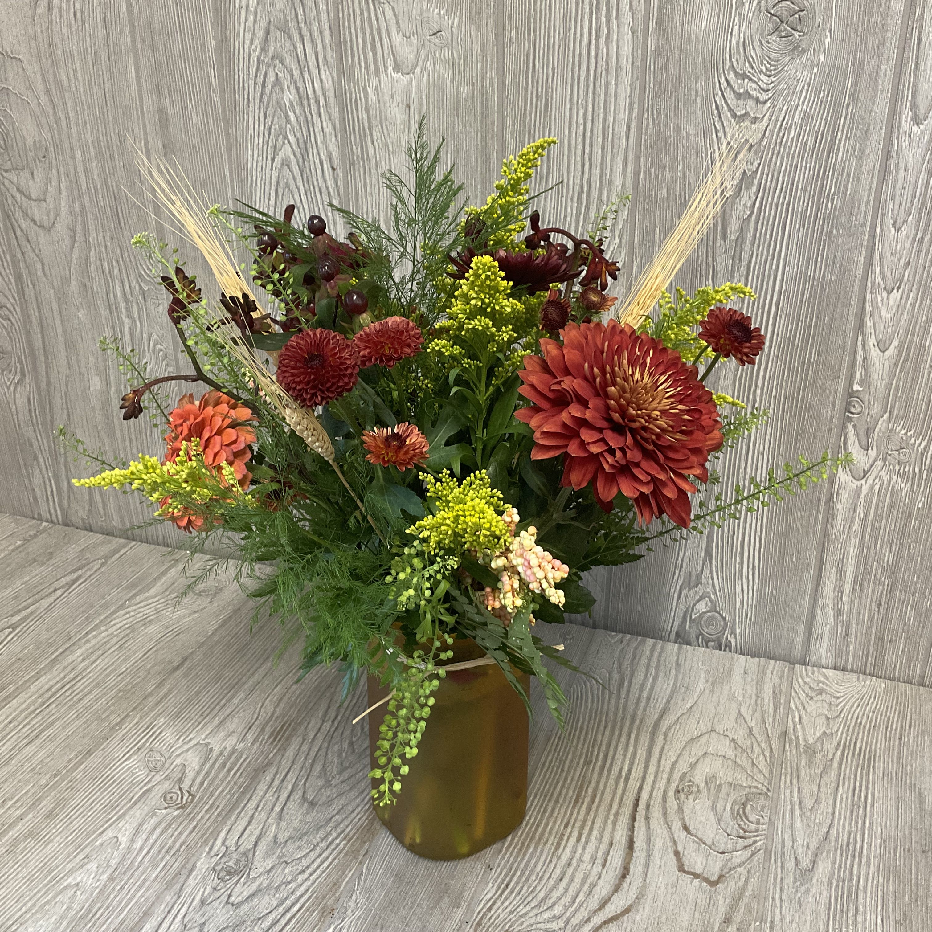 Mixed autumn bouquet in an amber vase with red and orange blooms