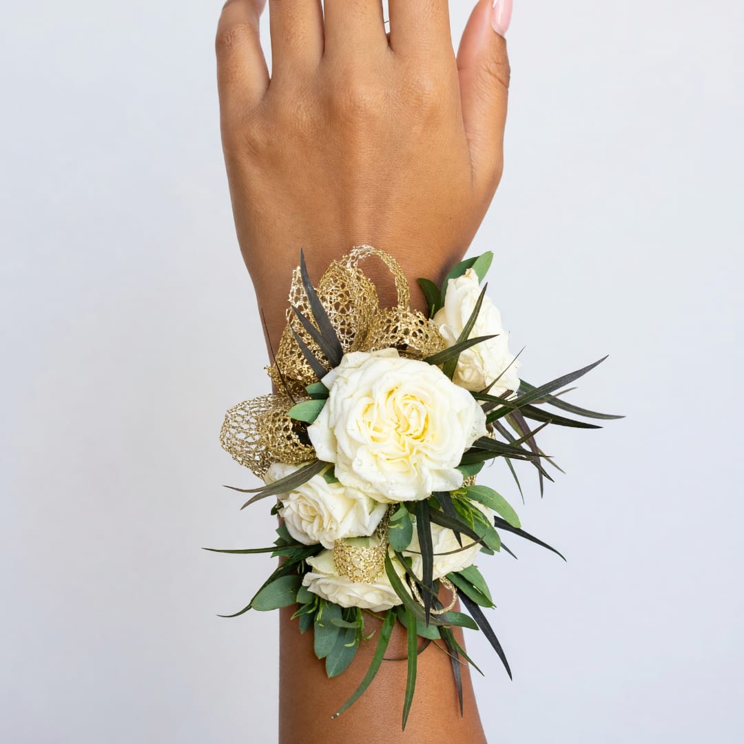 White rose wrist corsage with gold ribbon and greenery on a wrist