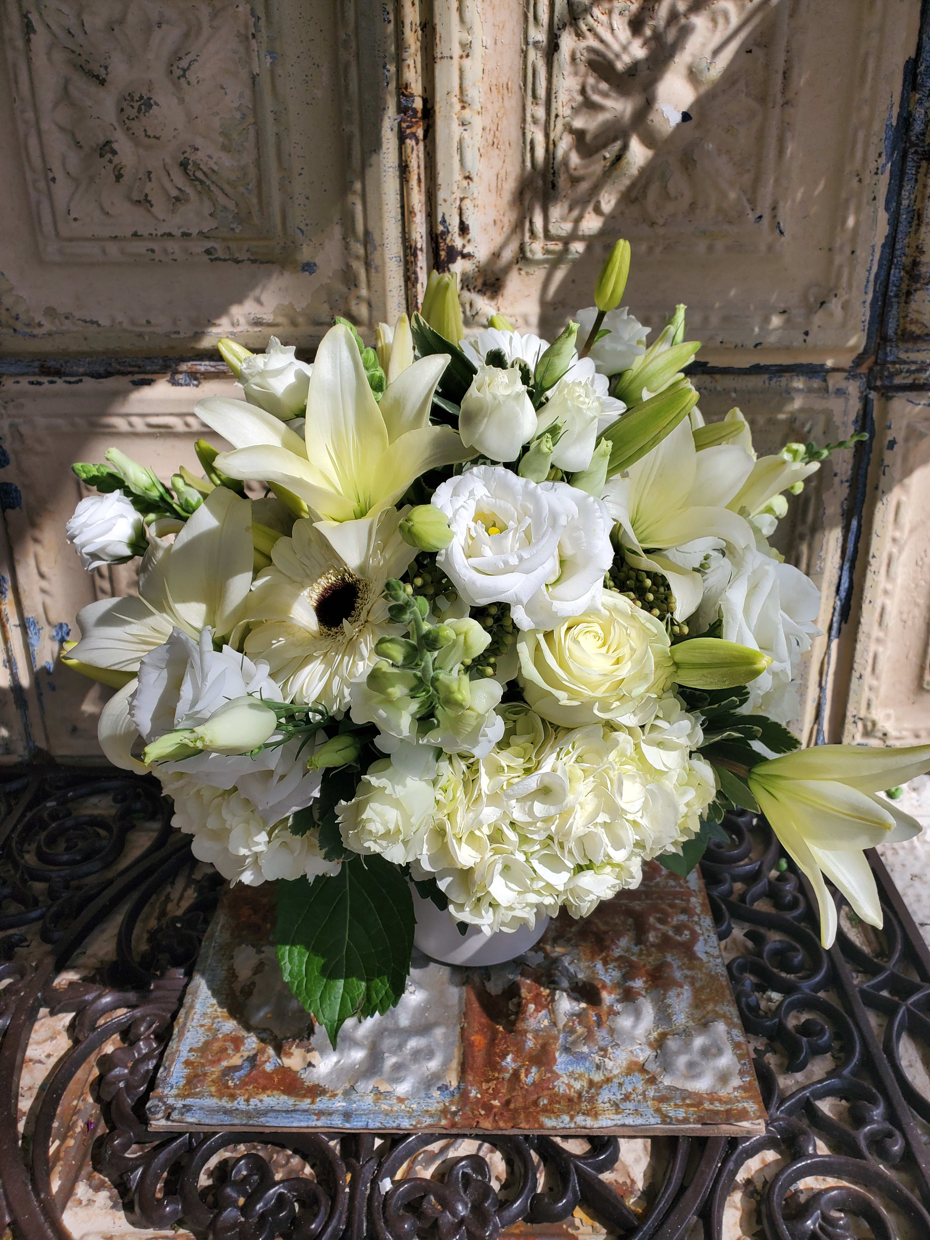 White floral arrangement with lilies, roses, hydrangeas, and a gerbera daisy in a vase