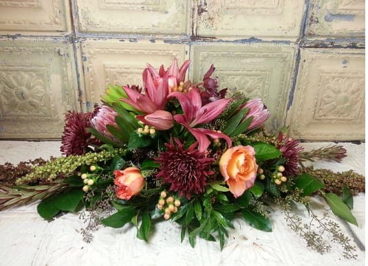Low floral arrangement with pink lilies, peach roses, and burgundy blooms