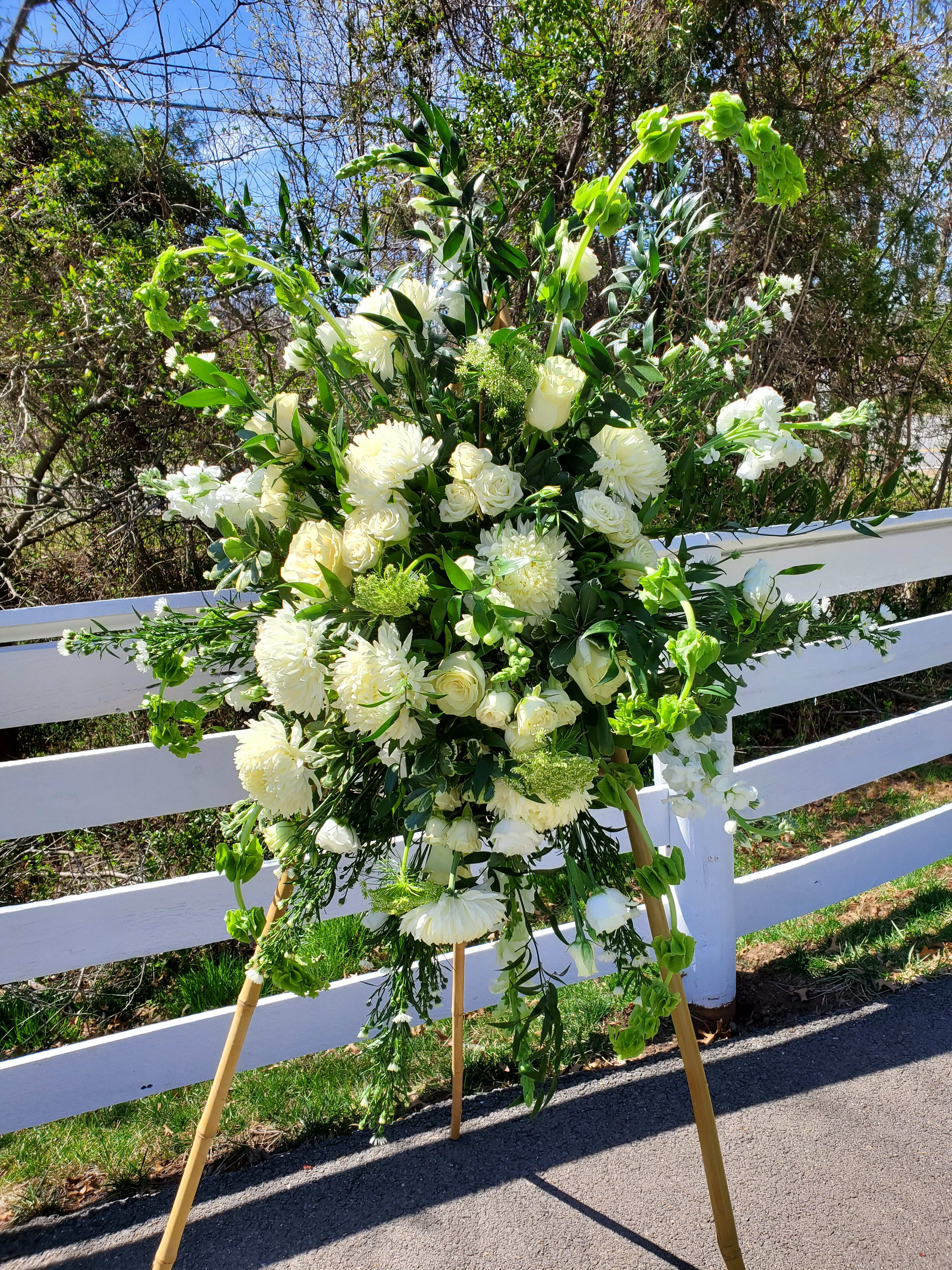 Resting Reston - White/green funeral easel featuring mums, roses, snapdragons, Belles of Ireland, daisies, and other foliage.