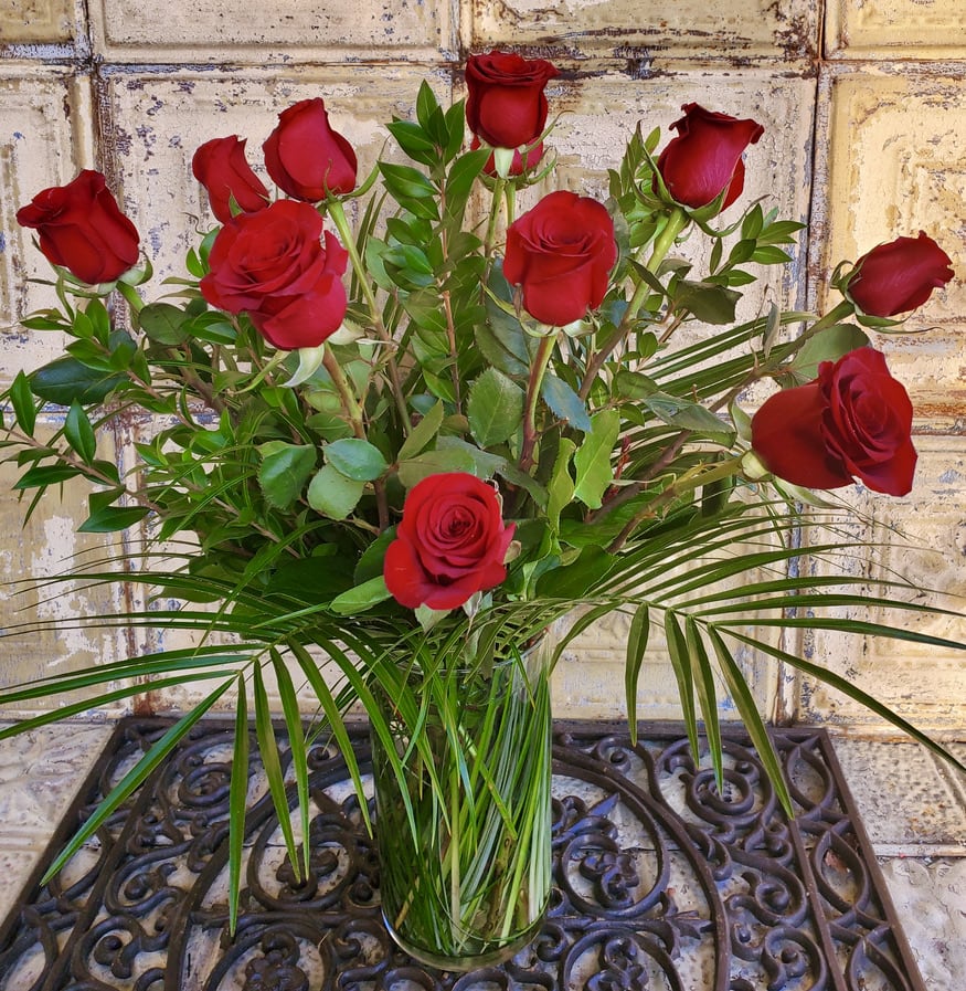 Red roses arranged in a clear glass vase with greenery