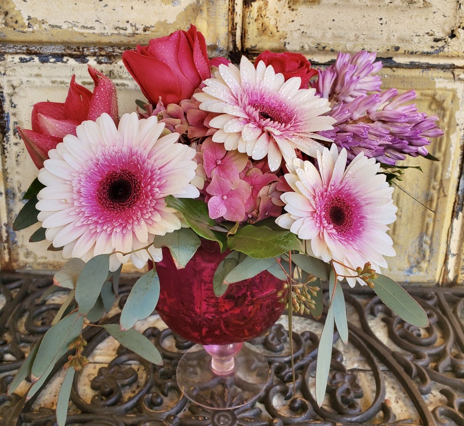Pink and white gerbera daisies with roses in a red glass vase
