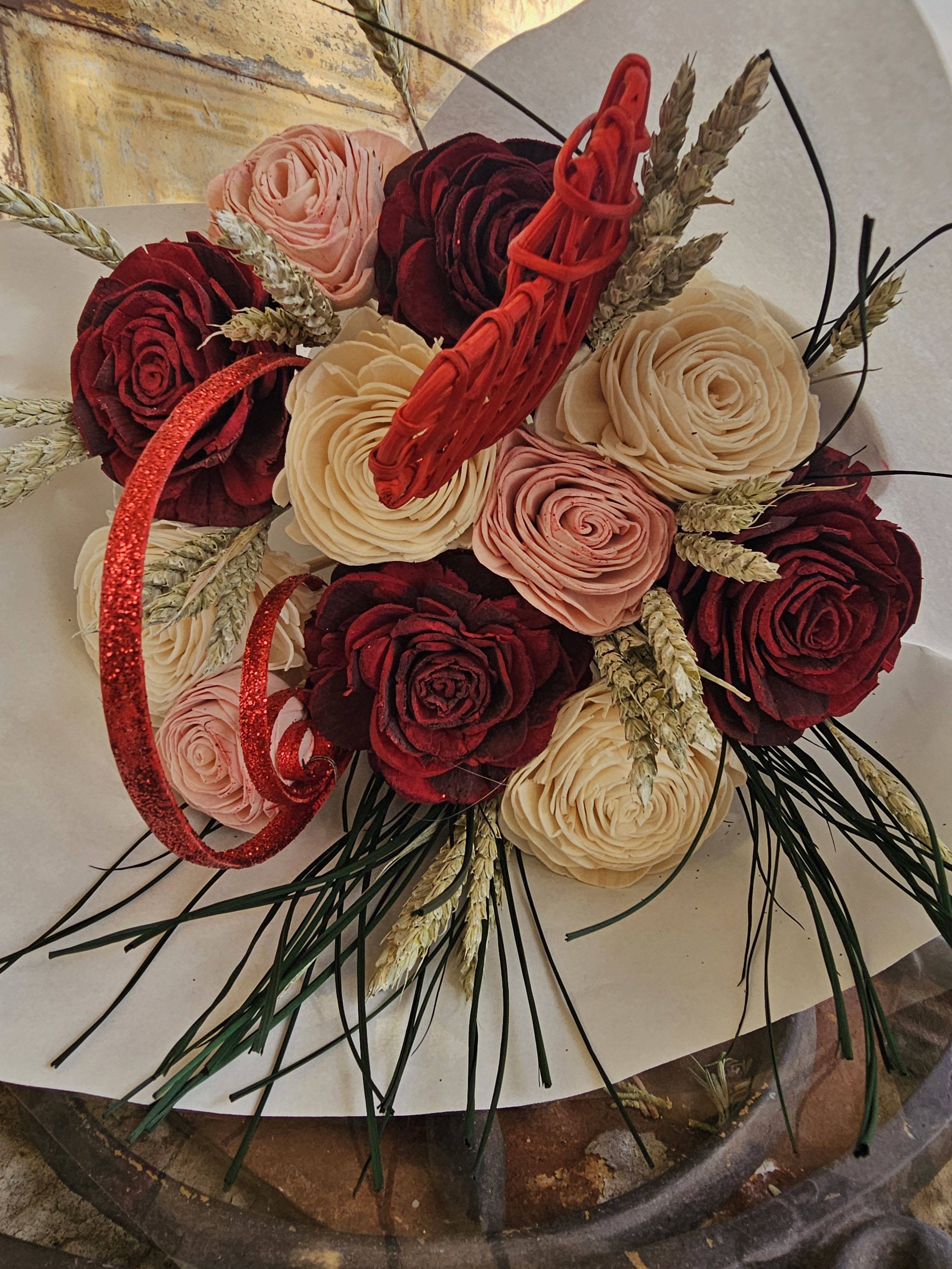Bouquet of red, blush, and cream roses with wheat and red ribbon accents